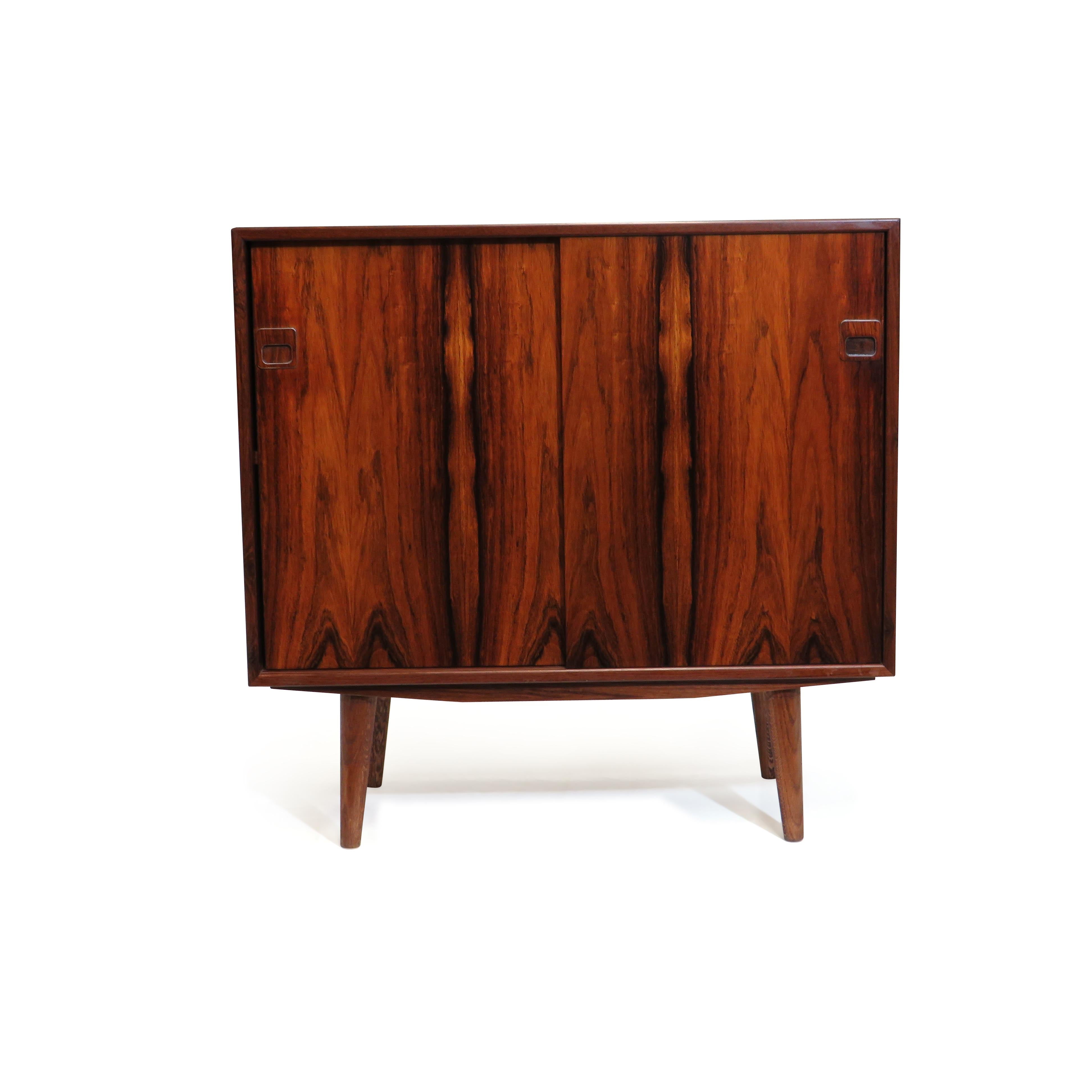 Pair of mid-century cabinets by Hjernebo, Denmark. Finely crafted with matching Brazilian rosewood grain, mitered corners, sculpted pulls with aluminum inlay, and raised on stained oak legs. Cabinet #1 features two sliding doors with an adjustable