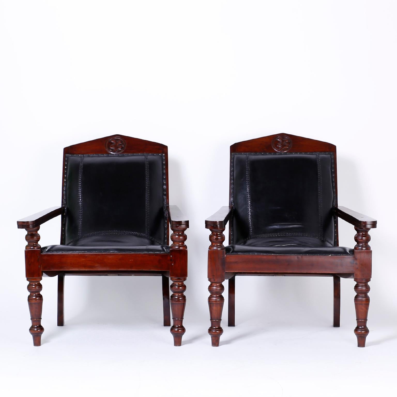 Pair of antique British Colonial mahogany plantation chairs upholstered in hand tooled black leather. The classic frames have a carved leaf on the crest, an elegant comfortable form, handmade pegged construction and fold out boot extensions. West