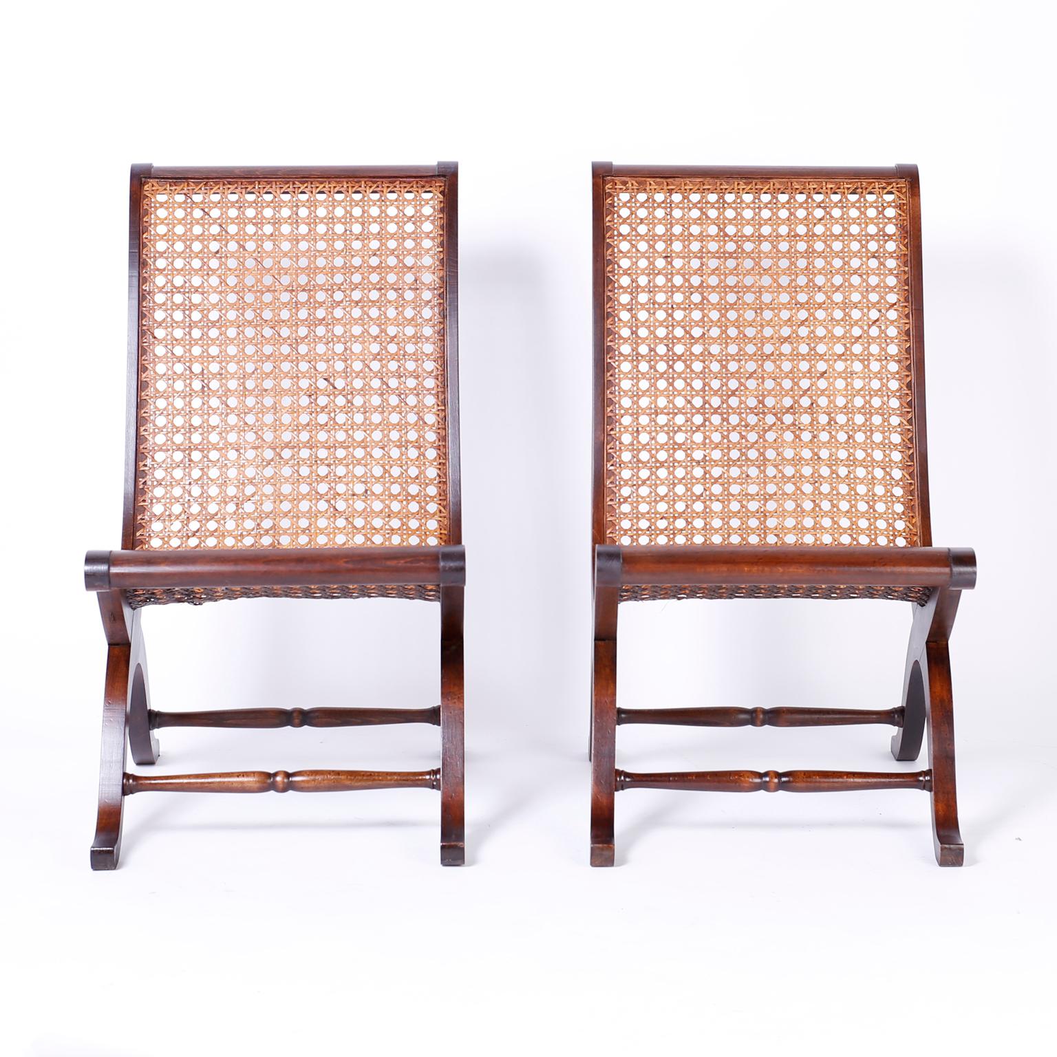 Pair of British colonial style Campeche chairs crafted in mahogany with a dramatic form, caned seat and back, saber legs and turned stretchers.