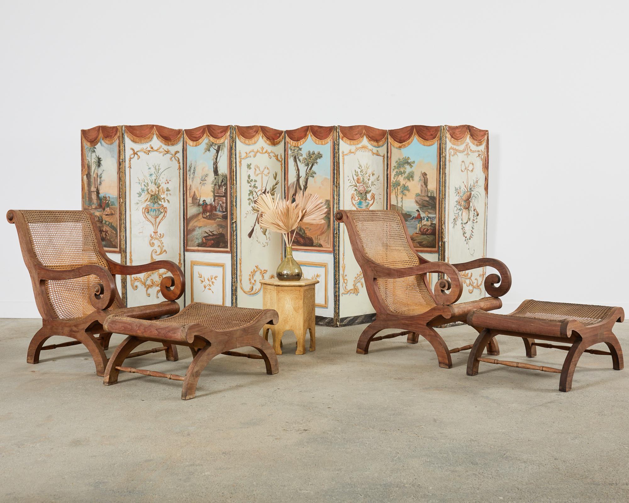 Gorgeous pair of Anglo-Indian plantation lounge chairs with matching ottomans made in the Grand British Colonial style. The chairs feature a gracefully carved teak frame with large scrolled arms. The seat and back is caned and the cane is intact.