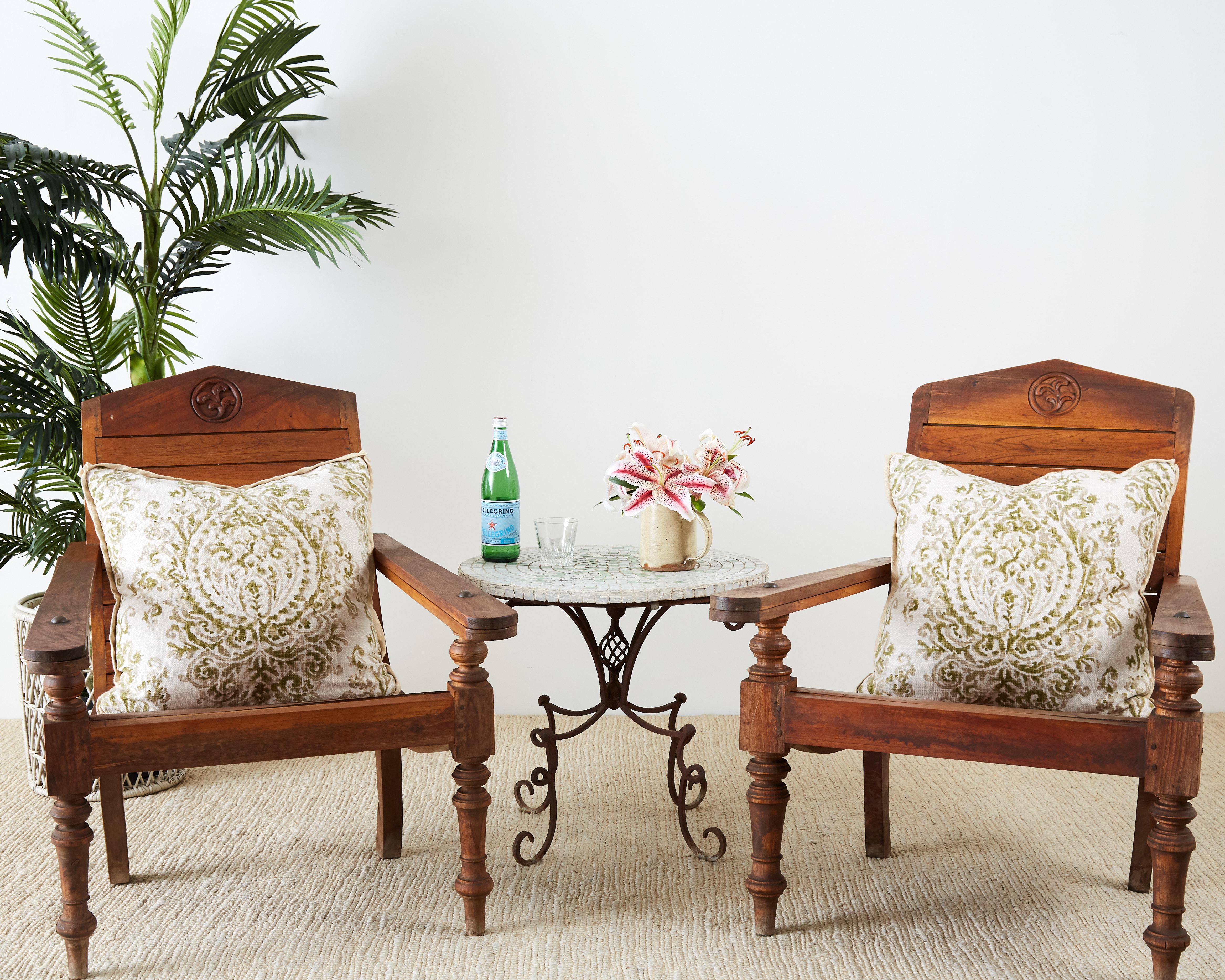 Handsome pair of hand carved teak plantation chairs made in the British Colonial style. Featuring fold-out leg supports and wood peg construction. Beautifully sculpted with a dramatic profile and ergonomic lounge seat. Supported by decorative turned