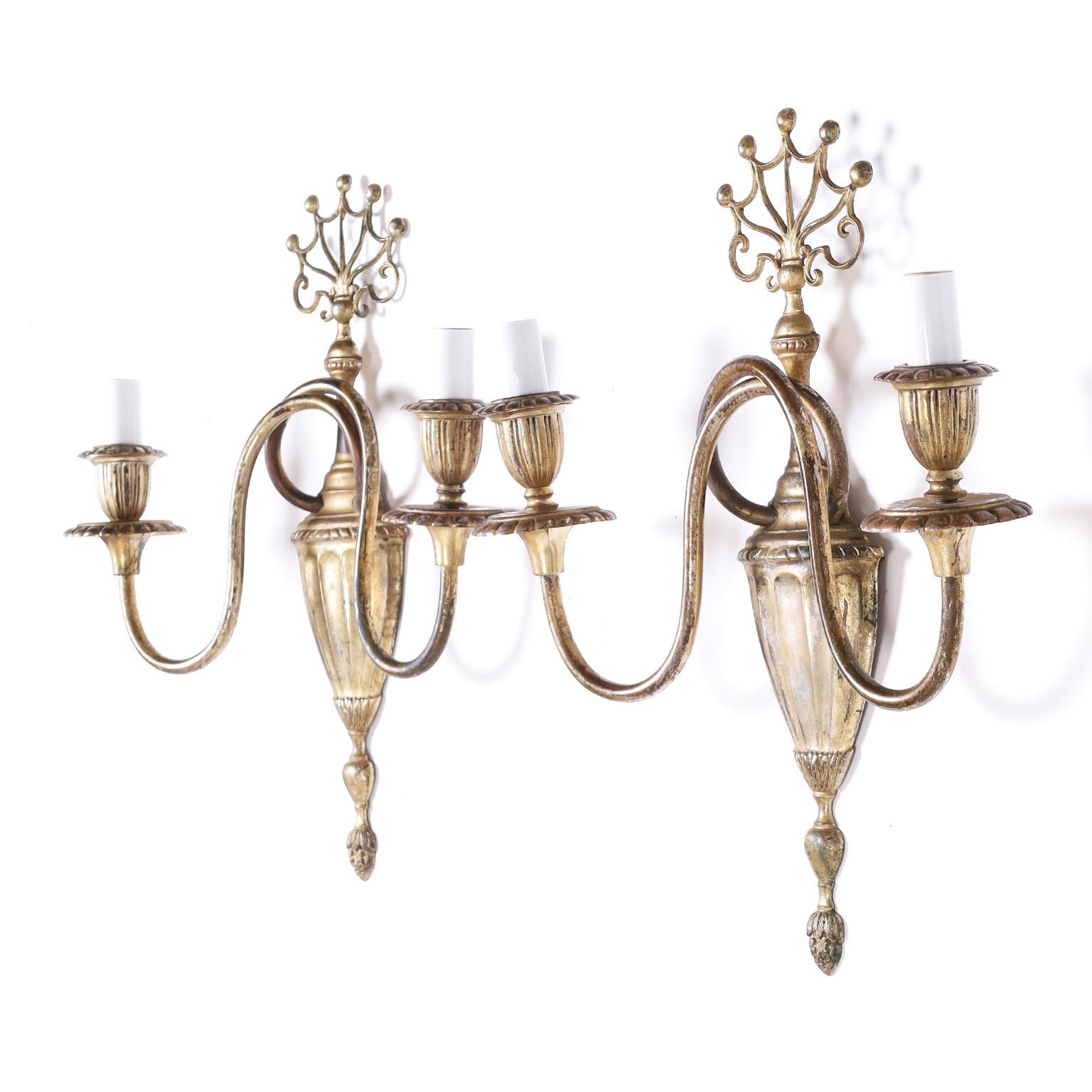 Pair of antique English wall sconces crafted in metal with a worn silver plate finish over a classic form having a crown, graceful looping arms, fluted urn, and an acorn finial at the bottom.