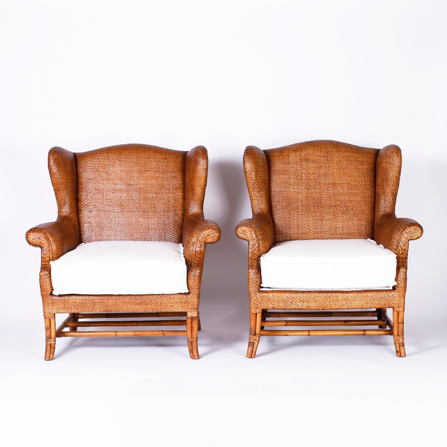 Pair of midcentury British colonial wing chairs with a classic form and bold scale crafted in wicker or grasscloth with removable linen cushions and bamboo splayed legs.