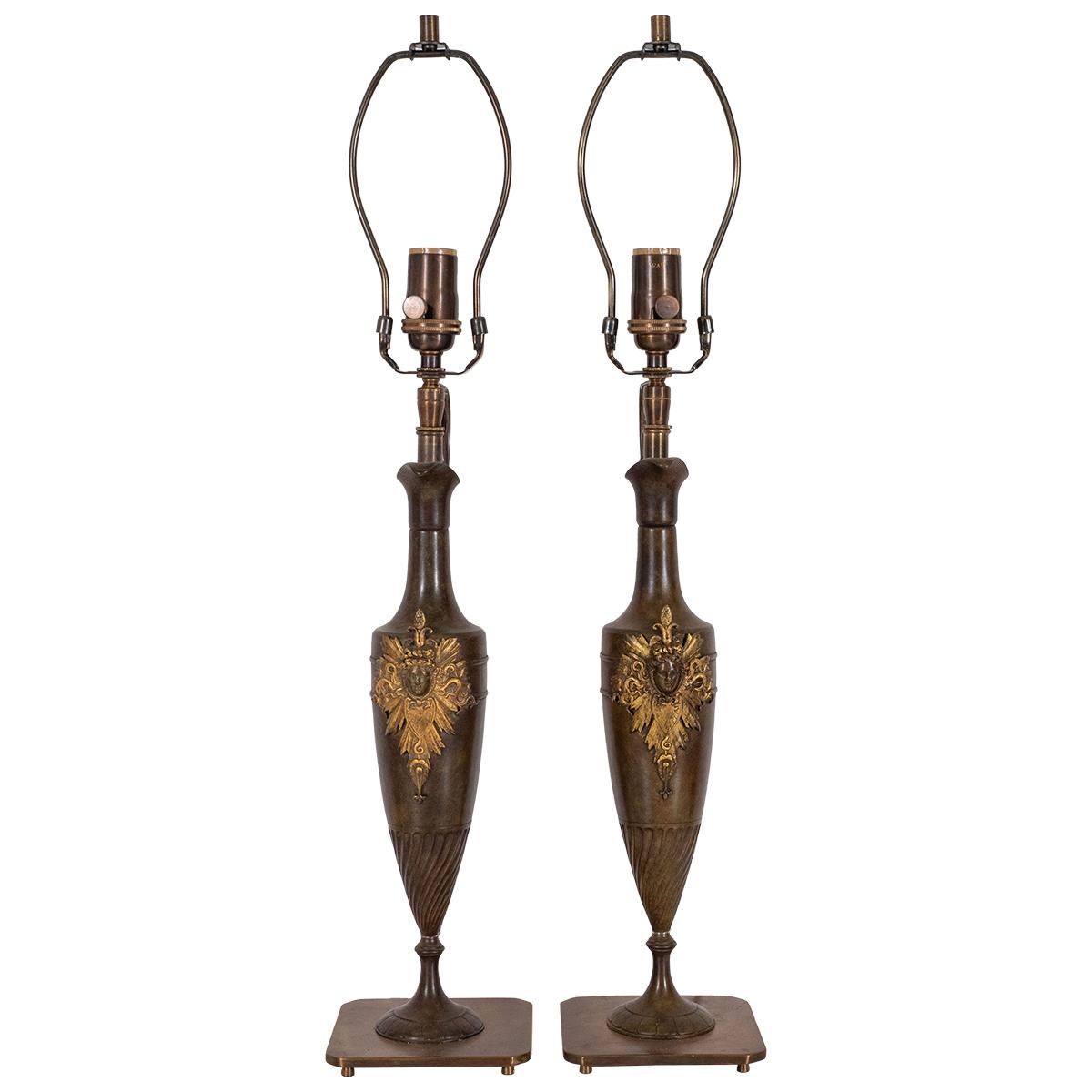 Pair of bronze amphora shaped tabled lamps with intricate gilt metal crests.
