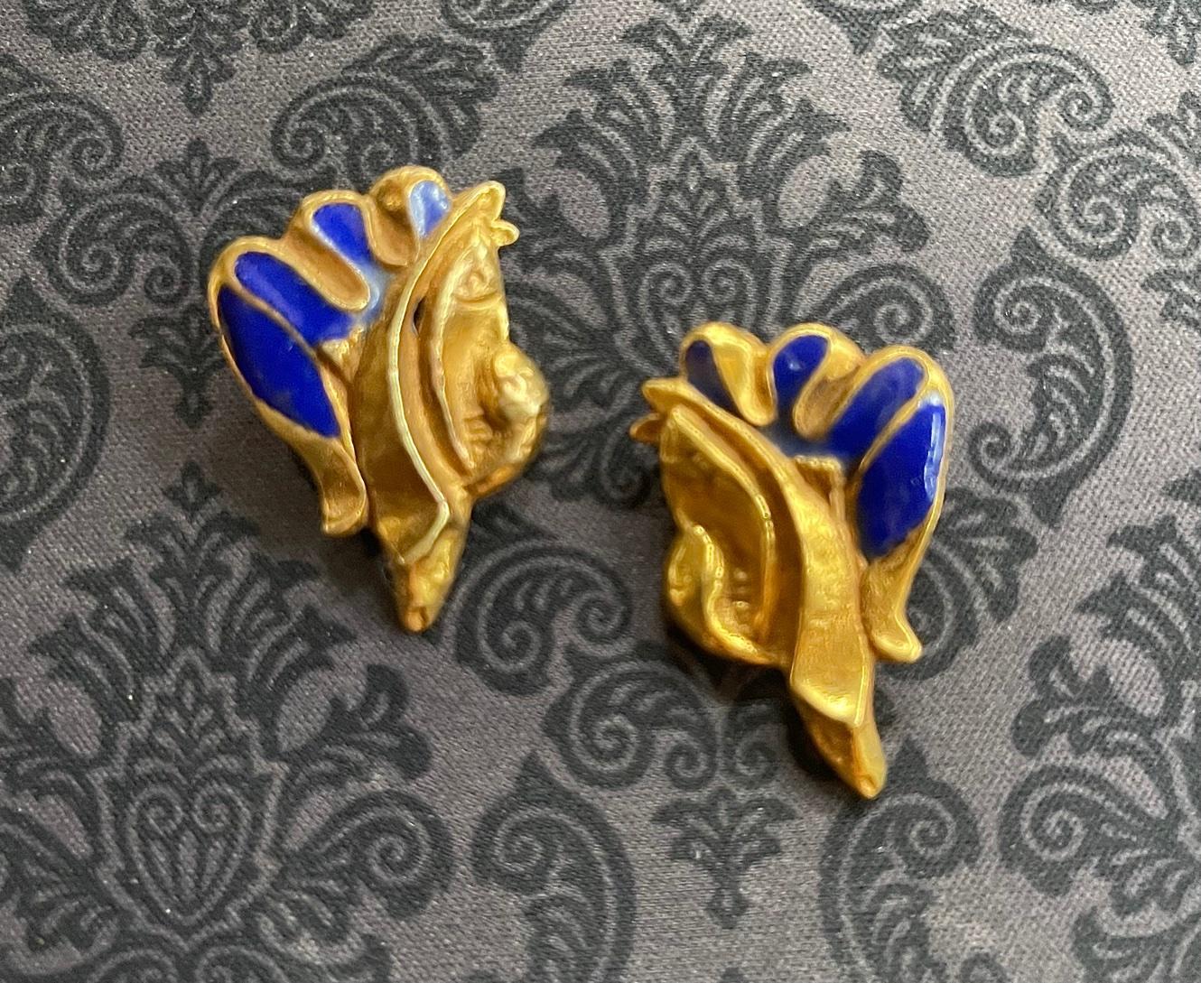 A pair of bespoken earrings by French Art Jeweler Line Vautrin (1913-1997). The cast bronze earring features a sculptural design that evokes an archaic form with shell like scroll and wing-like spread decorated with a cobalt blue enamel surface.