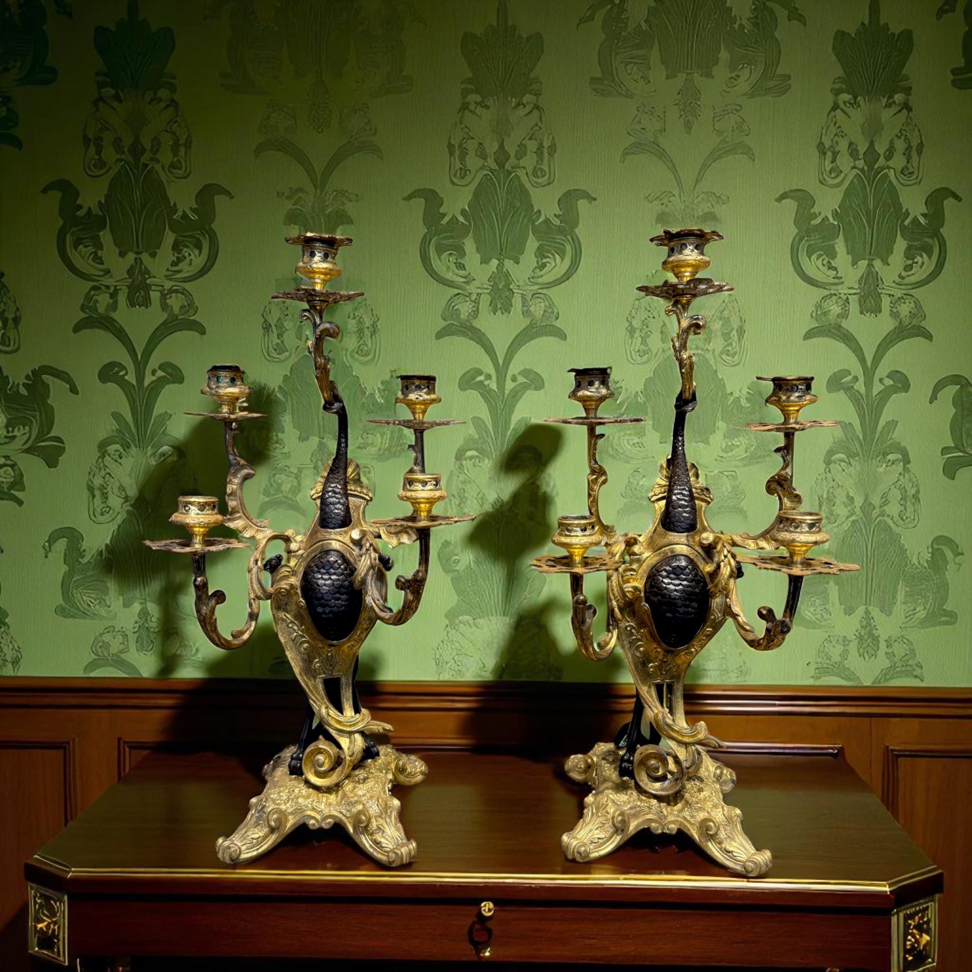 Esta pareja de candelabros franceses del siglo XIX está hecha de bronce patinado oscuro y bronce dorado brillante (ormolu). Cada pieza presenta una criatura mítica, posiblemente un dragón o una quimera, erguida y sosteniendo cinco candelabros con