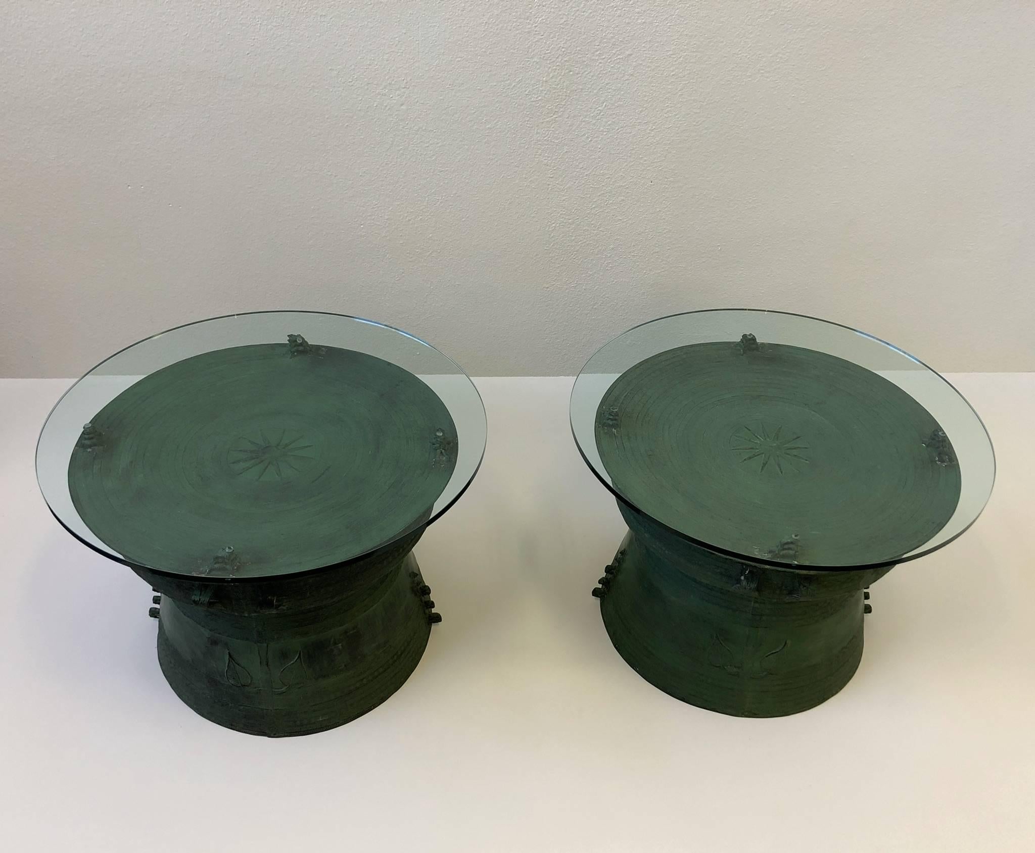 An amazing pair of cast bronze with glass tops, south Asian rain drum side table. The tables have a beautiful aged patina to them. They are decorated with a star on the centre of the top and four sets of triple stacked frogs that hold the glass up.