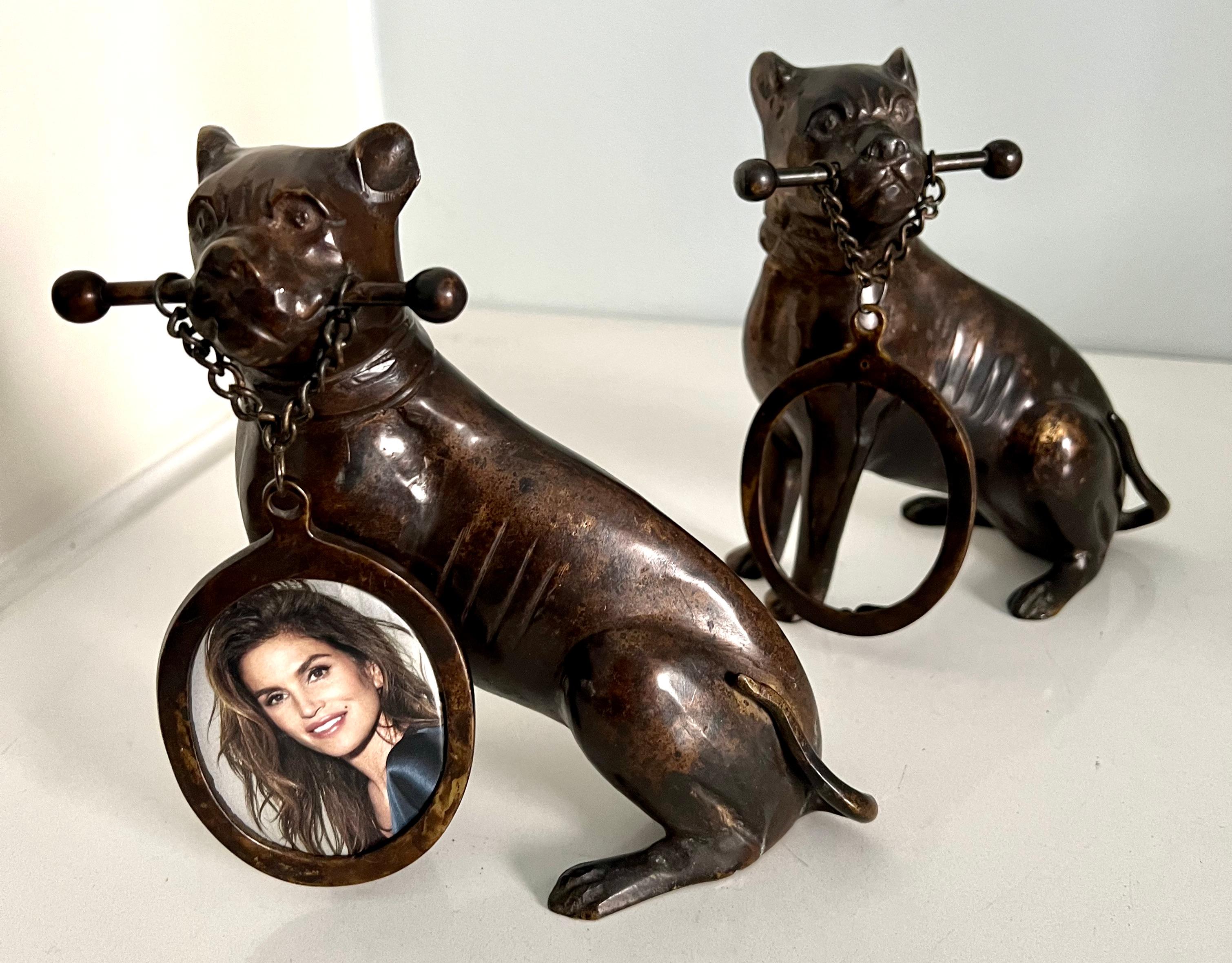 Una coppia di fermalibri o sculture di cani davvero unica, che tengono in bocca una cornice ovale proveniente da un palo incatenato... la coppia può stare in piedi indipendentemente o essere usata come fermalibri - in ogni caso il loro ovale di 2
