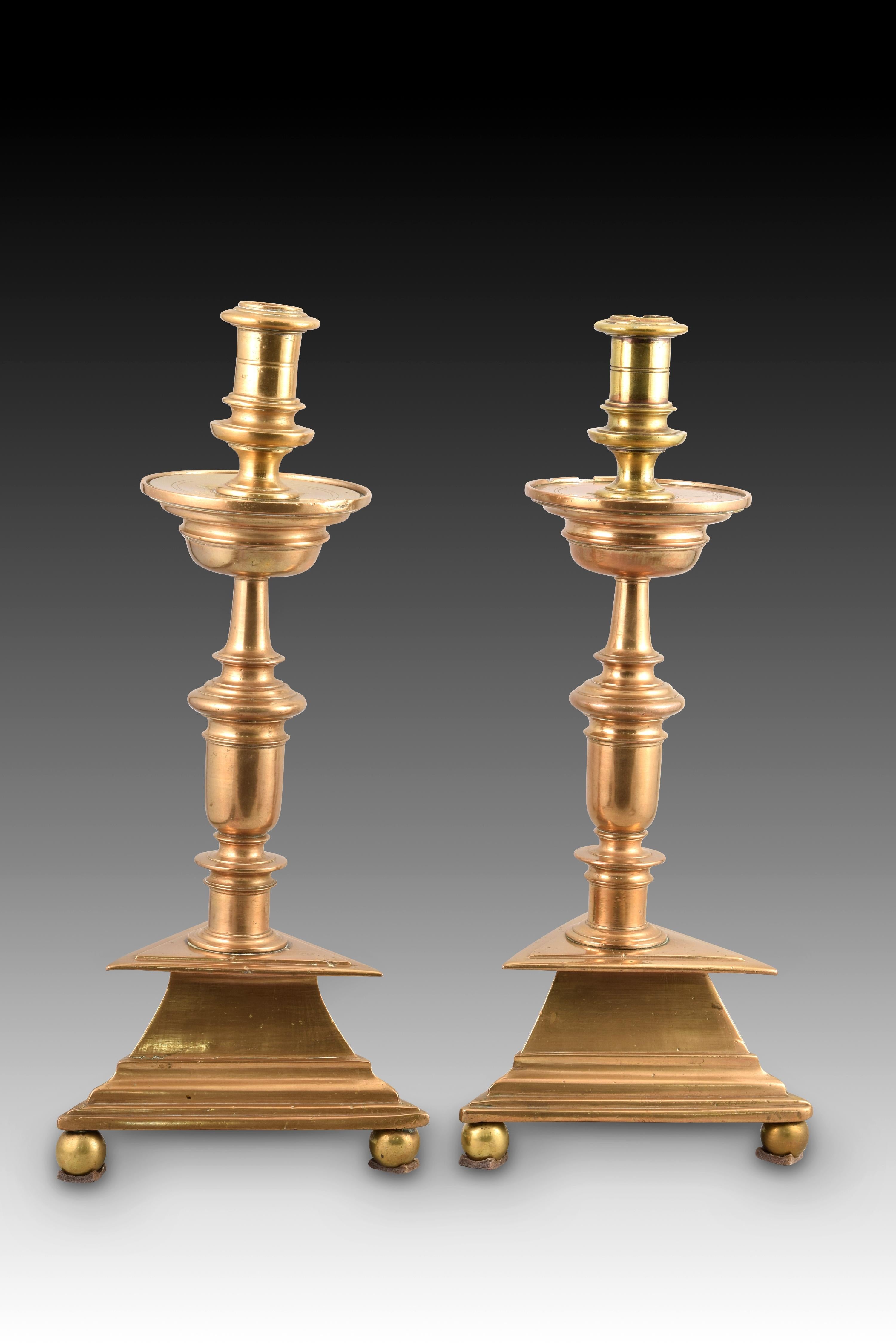 Pair of candlesticks. Bronze. XVII century and later.
Replaced stem. 
Pair of bronze candlesticks raised on three legs, with triangular bases and enhanced with ready moldings, turned stems with architectural profiles of classicist airs and circular