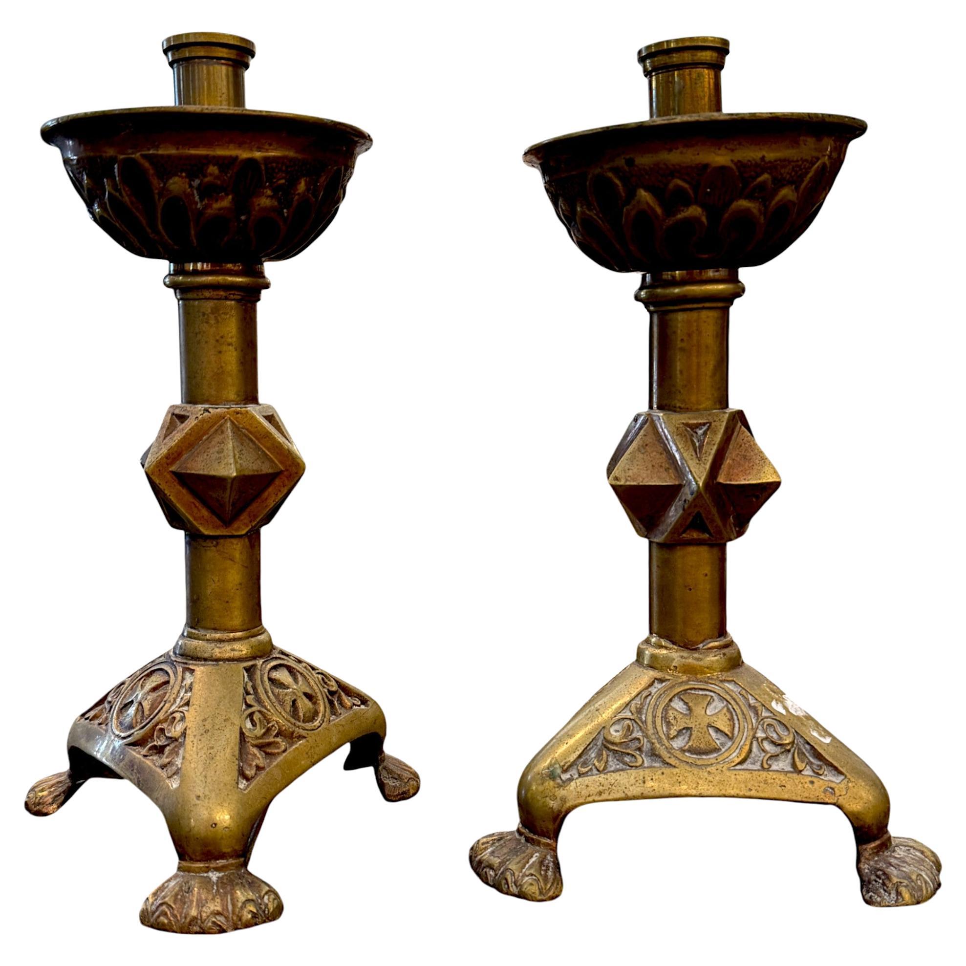 A pair of 17th-century bronze candlesticks featuring architectural details. Each piece is crafted from heavy cast bronze and displays intricate floral and geometric motifs, including a raised cross enclosed in a circle on each leg.

The stems are