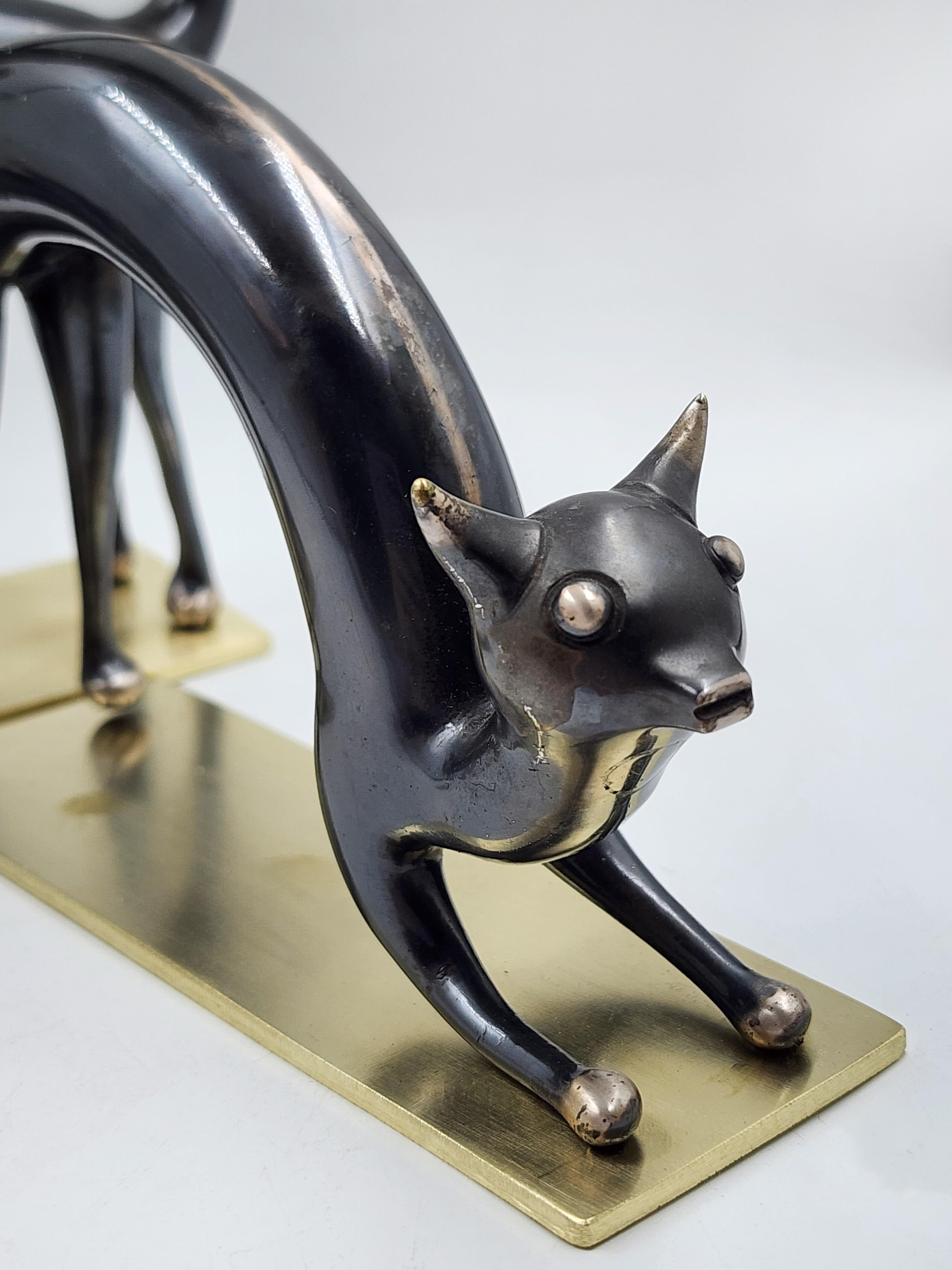 Pair of Viennese Bronze Cat Bookends by Hagenauer
This pair of bookends features a stylized bronze cat design by Hagenauer, Vienna. Each cat is depicted in a stretched pose, with their bodies arched and tails elegantly curved. Details include