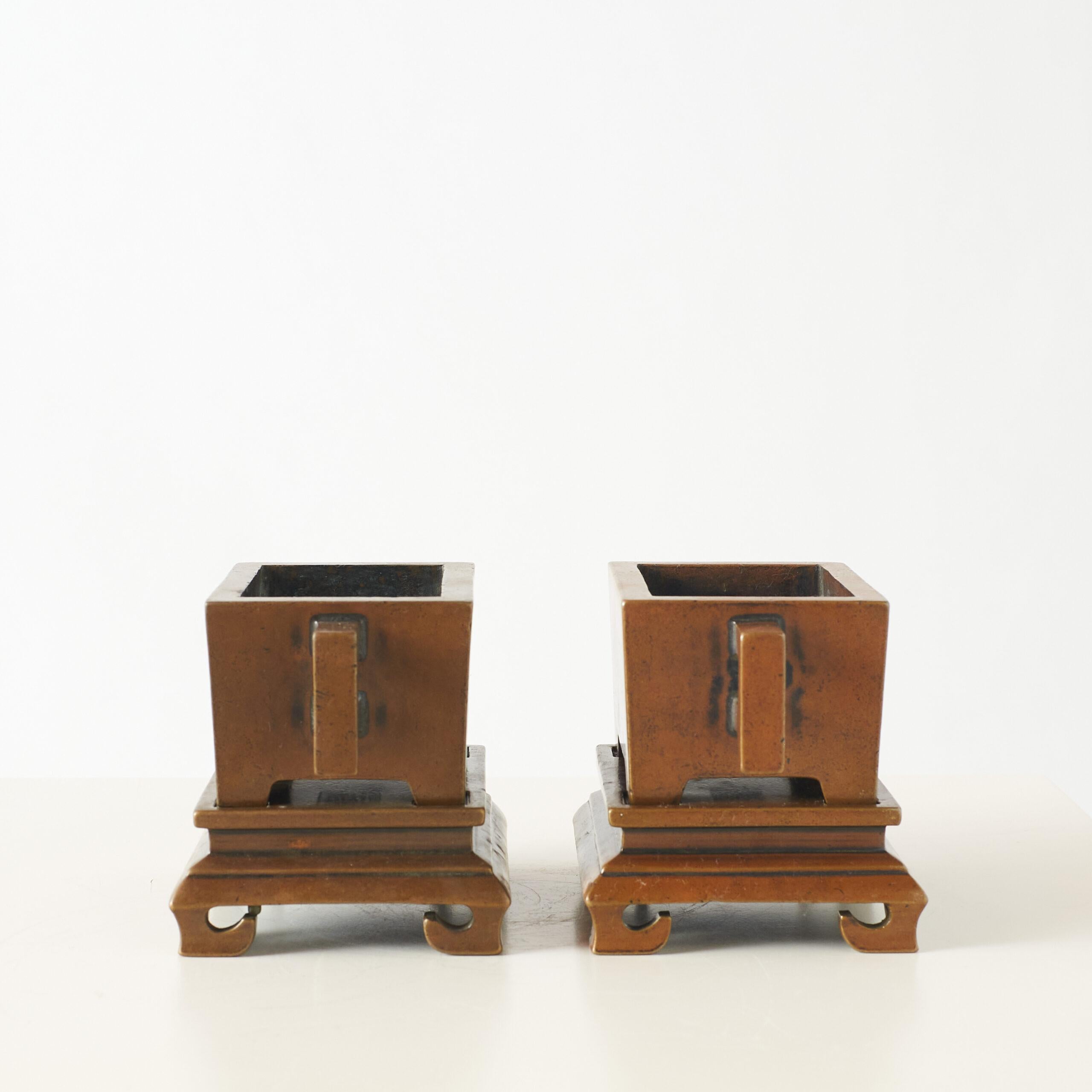 Pair of Bronze Censers on Carved Bases, Marked “Qin Shu Lu”

A pair of antique Chinese bronze censers with square bodies, upright handles, and finely carved bases. The surfaces have a warm, aged patina. The inscription “琴书炉” (Qin Shu Lu) on each