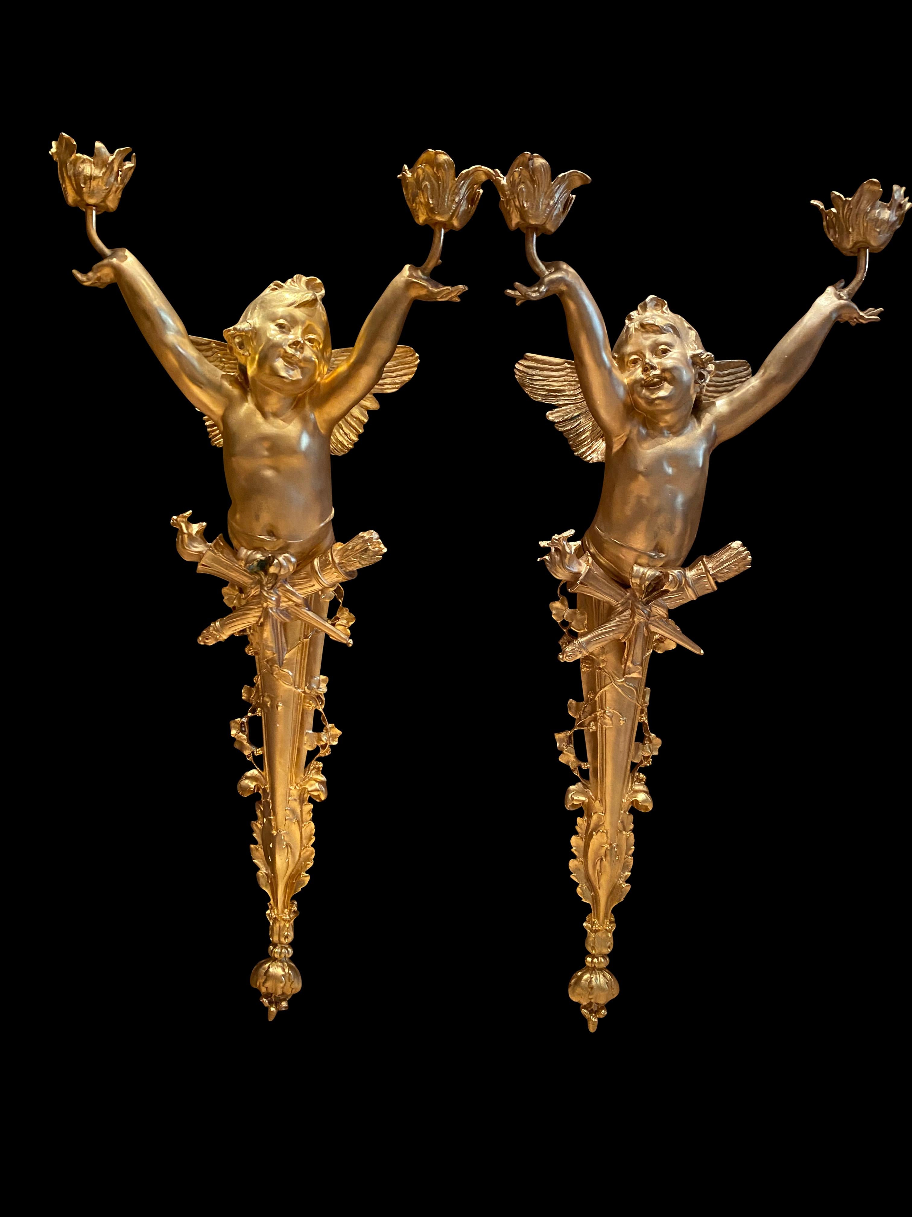 A pair of bronze cherub torchères/wall sconces, 20th century. Each cherub holds a cup decorated in petals, with a crossed torchère and arrow sheath. Perfect for home decoration.