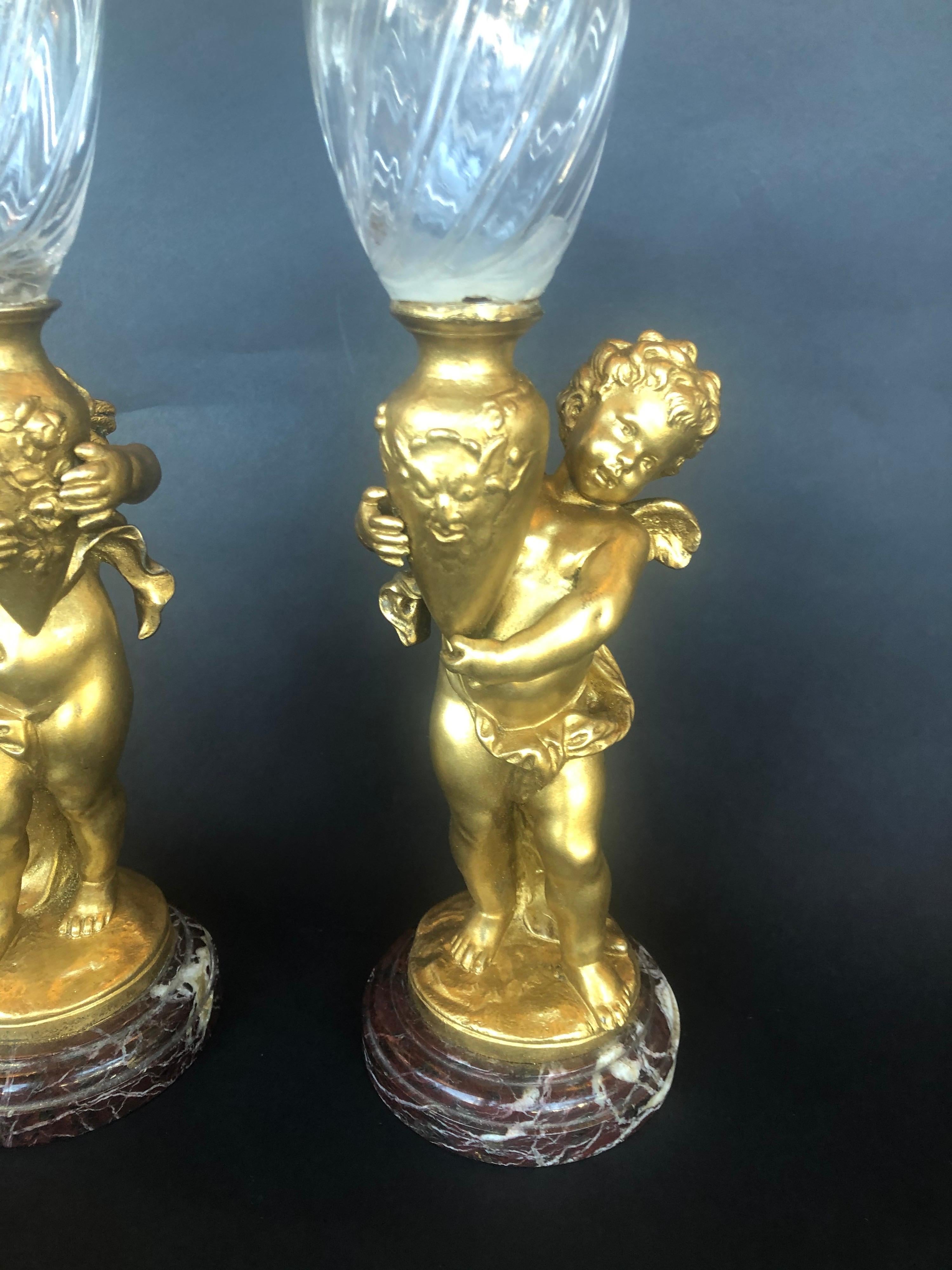 Two bronze cherubs on a marble base holding glass vases.