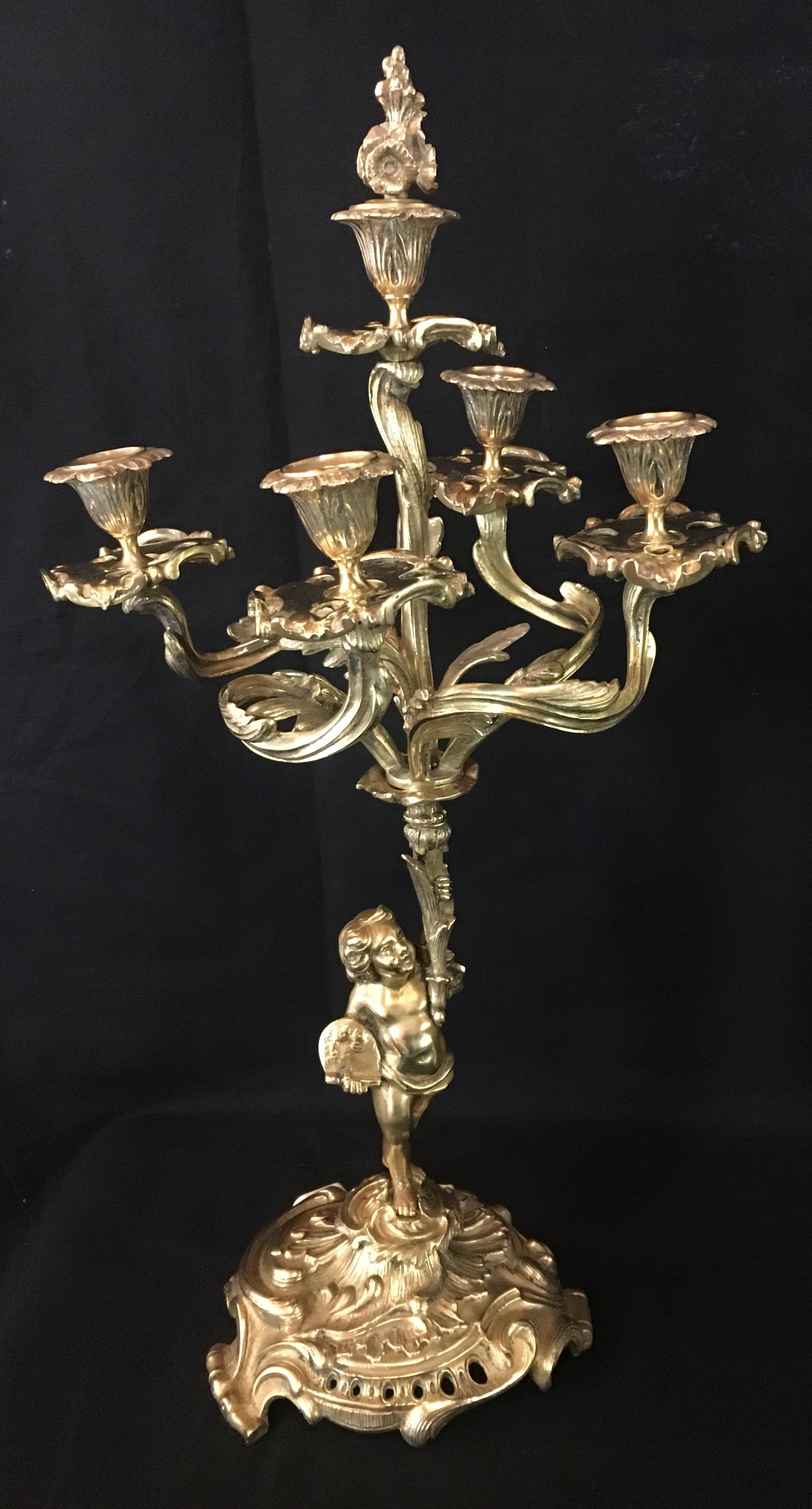 A very fine pair of French 19th century Louis XV style figural bronze and five-armed candelabras, each with a figure of a standing cherub holding the ornate scrolled arm candelabra, crowned with a bronze candle snuffer in the shape of a burning