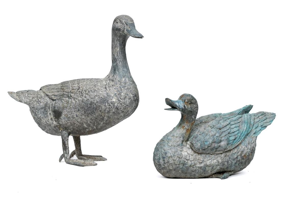 A Vintage Pair of Bronze Ducks with fine detail and lifelike appearance. One goose is recumbent the other stands. Each with finely detailed feathers and painted in a pale verdigris tone. 

Dimensions:
14 1/2