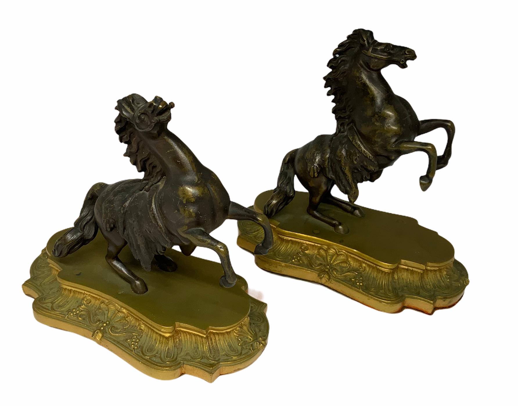 A pair of patinated bronze bookends depicting rearing horses figurines resting on a gilt bronze Rococo base.
