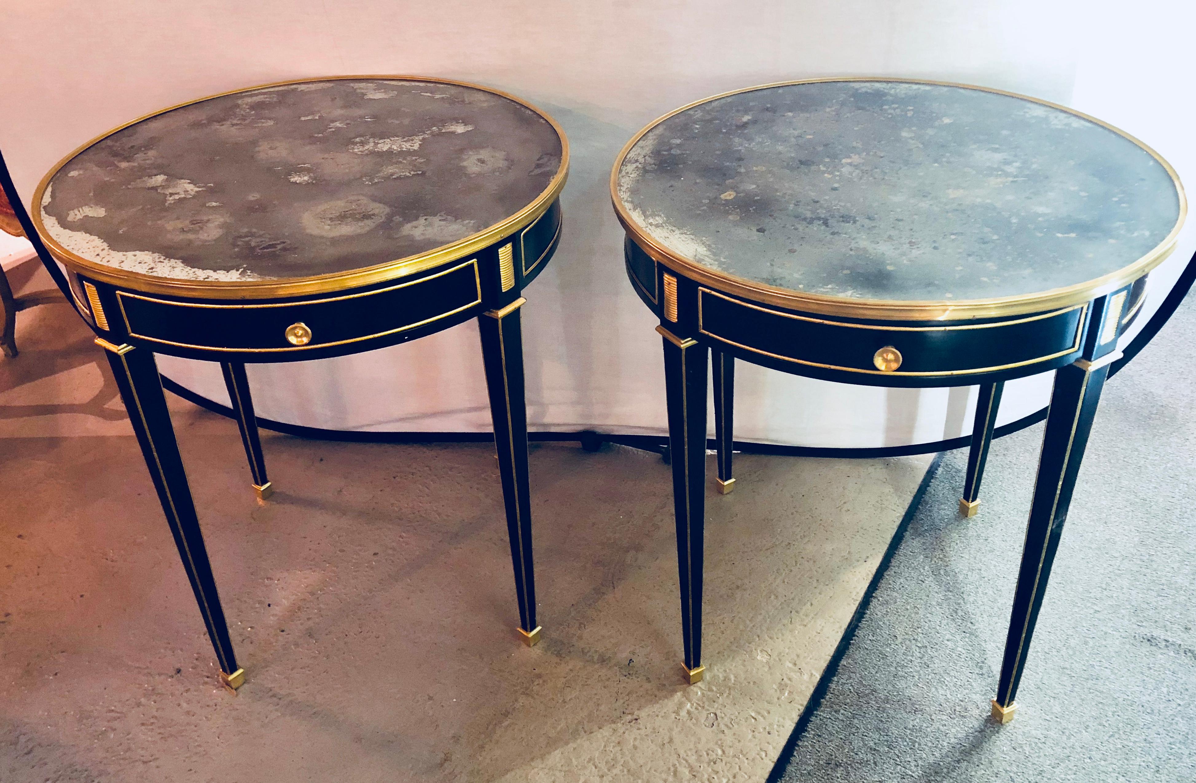 Pair of bronze mounted ebonized bouillotte or end tables having mirror tops in the Maison Jansen style. Each Louis XVI inspired end table having a set of bronze sabots leading to tapering legs all with bronze reeded trimmed corners terminating in
