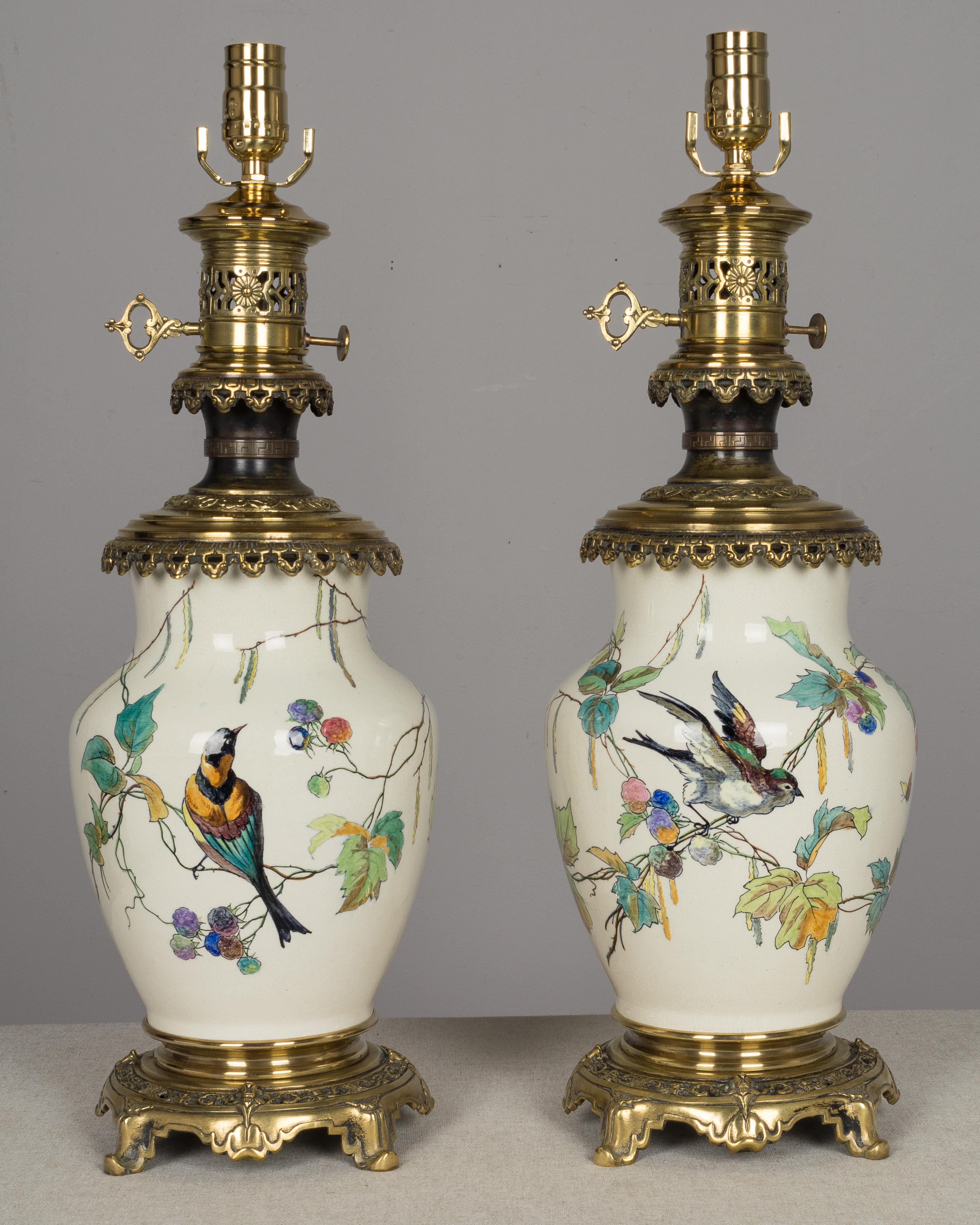 A pair of rare 19th century French bronze-mounted Sevres ceramic lamps, beautifully hand painted by Charles Ficquenet in the manner of Theodore Deck. Four different birds, each painted in colorful detail, perch on branches with pale green leaves and