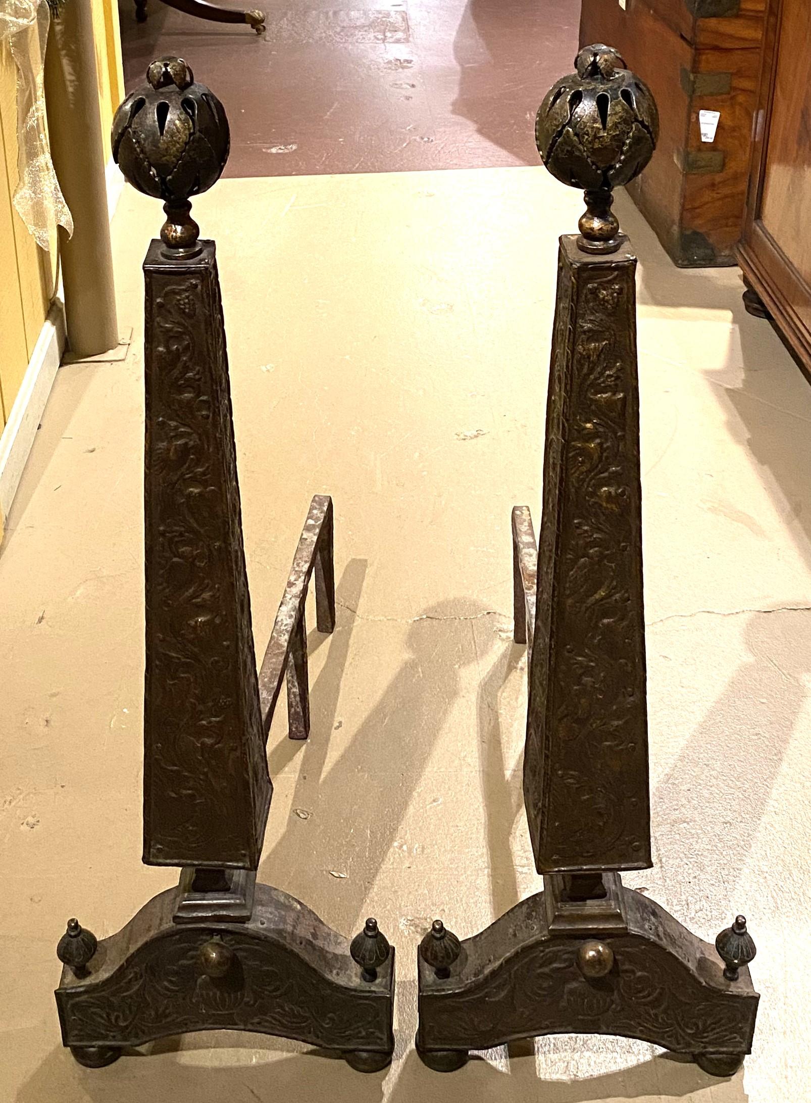 A nice pair of bronze obelisk form Arts & Crafts andirons with foliate relief decoration, reticulated ball finials, and great overall patina. The pair date to the early 20th century and are in very good condition, with some light rust on the dogs,