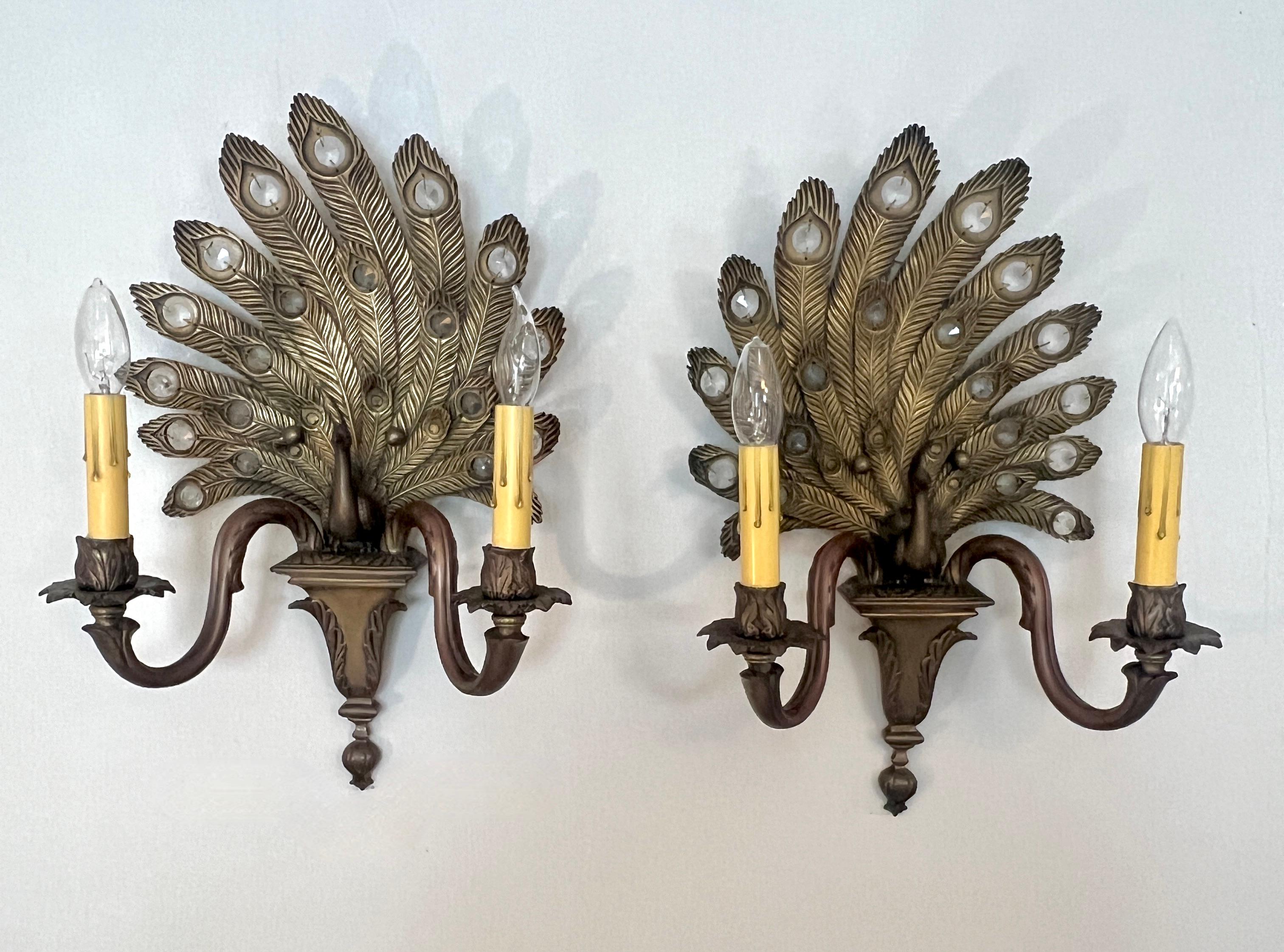 Precioso par de apliques de bronce hechos a mano con forma de pavo real con penachos.  Cada penacho tiene un cristal adosado para añadir más brillo con las luces encendidas.  

Los penachos se mueven en direcciones opuestas dando atención a una