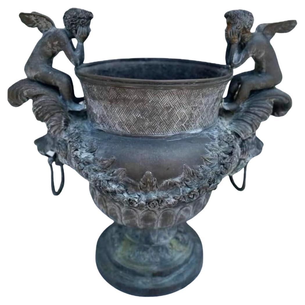 A pair of very prolific Bronze planters flanked by opposing Cherubs with bold lion faces and rings.

The pair are a compliment to any entry way or garden setting along a walkway.  The patinated bronze shows great signs of age that can only be