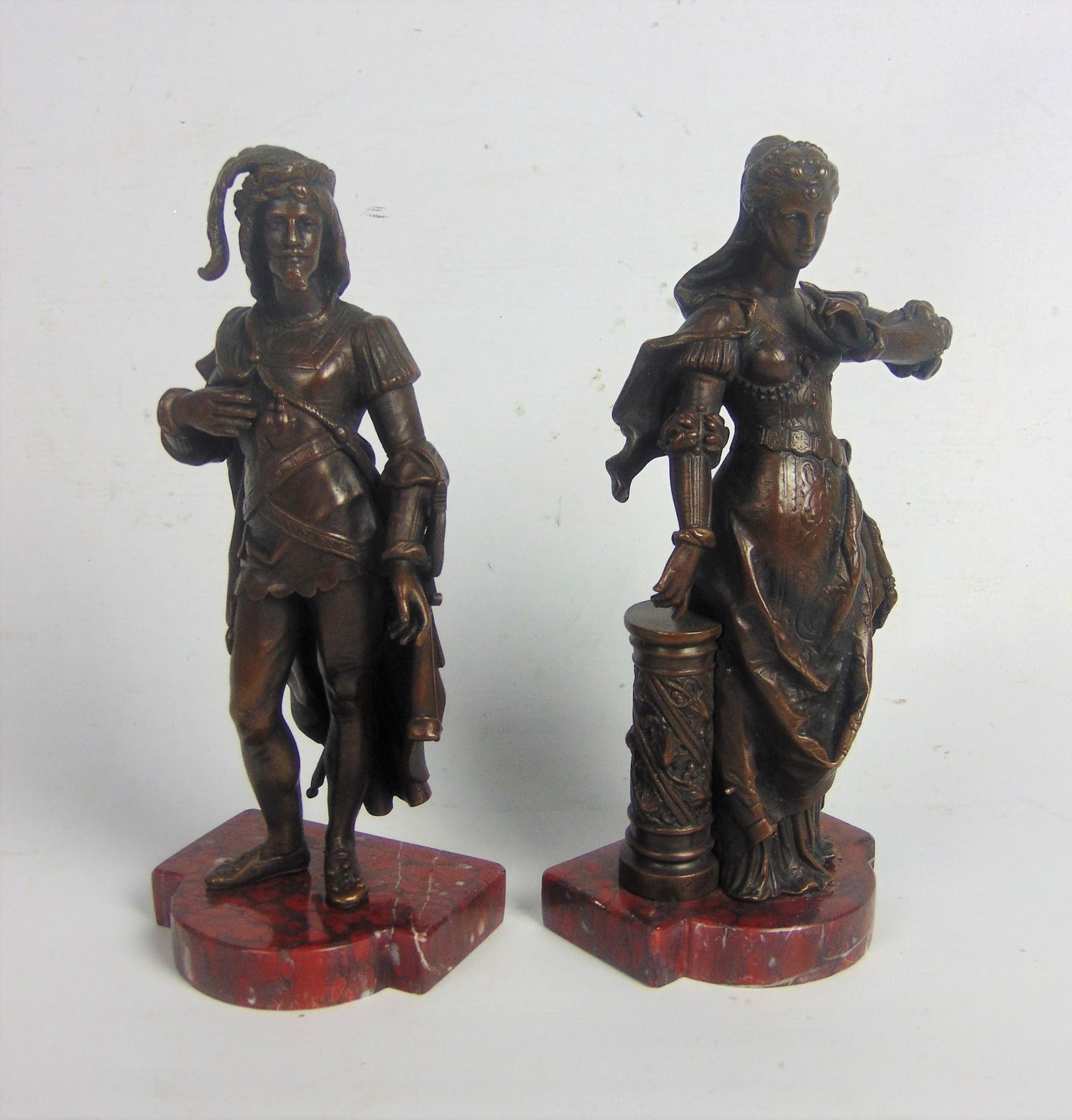 Une belle paire de bronzes portant chacun un costume médiéval, la dame dans une longue robe brodée des plus élégantes, les cheveux attachés, et l'homme à l'allure élégante, manteau sur l'épaule et épée à la main gauche, sur des socles en marbre