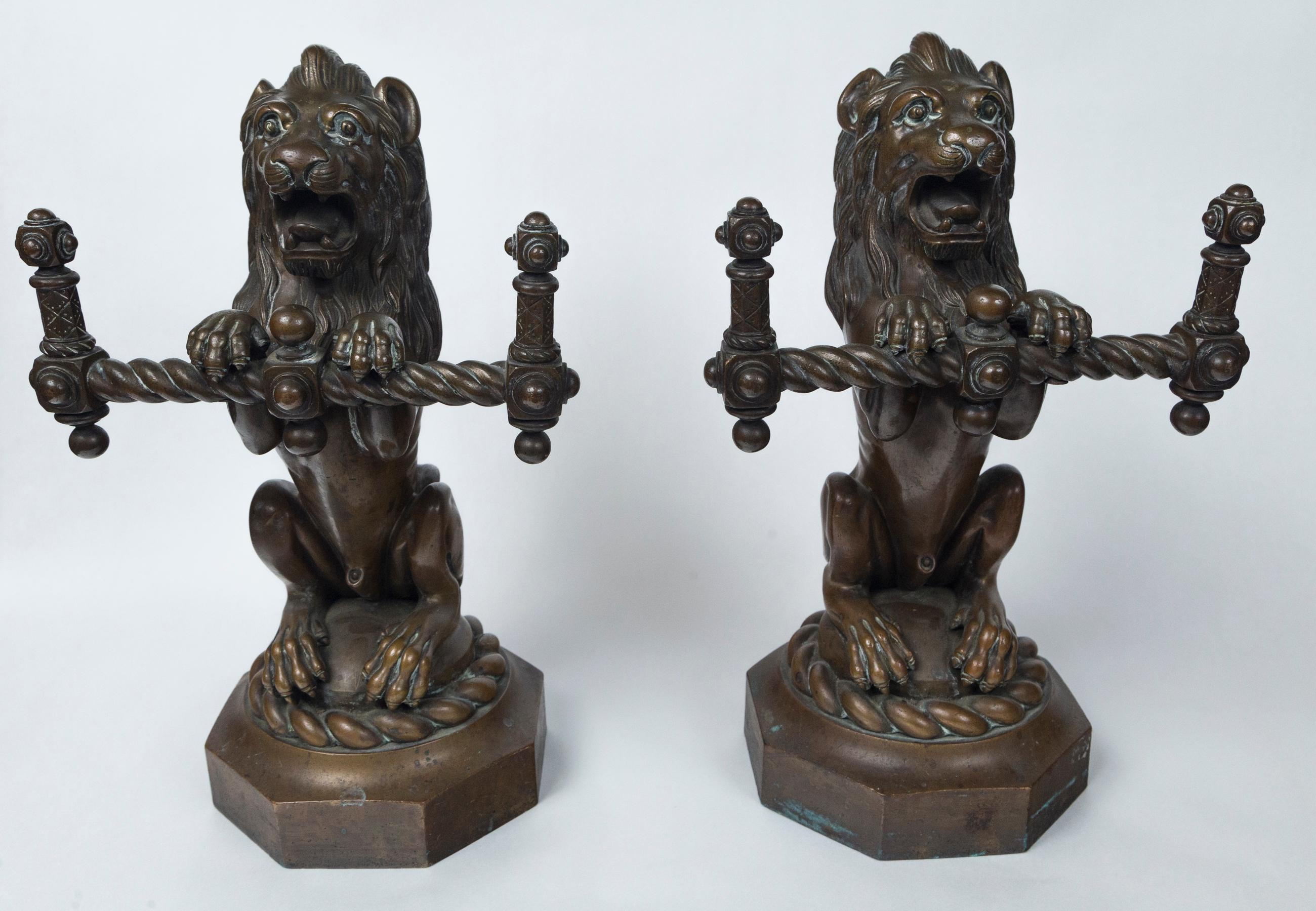 An usual pair of bronze lions, sitting on their haunches, upon an attached 6 sided cast bronze base. The base is 1.5 inches in height and measures 6 inches in diameter. The overall height is 14.5 inches.
Each lion holds a horizontal bronze bar,