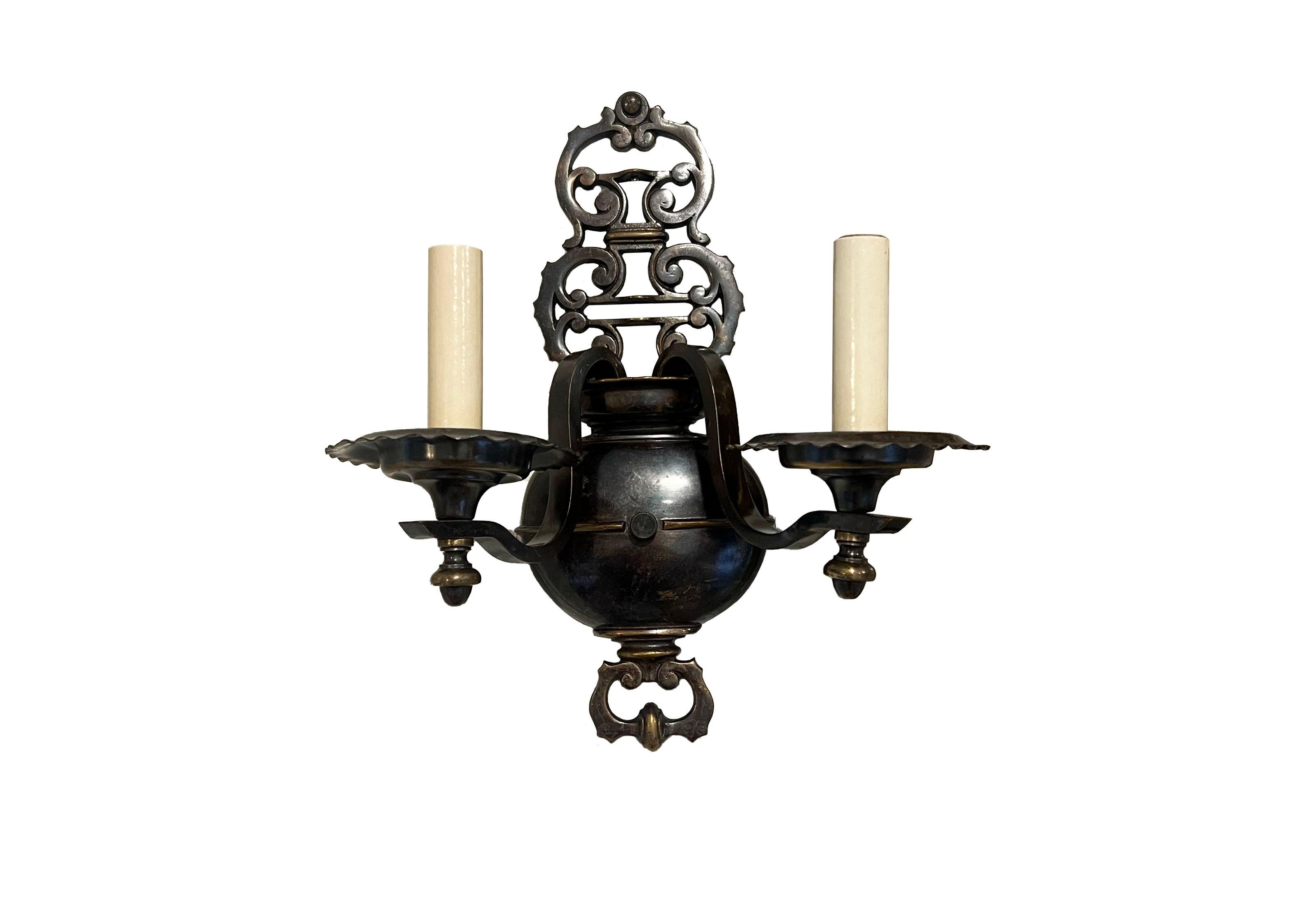 A pair of two-light sconces. Crafted with exquisite attention to detail, these sconces feature a patinated bronze metal finish that exudes a warm, inviting glow, perfect for creating a cozy ambiance in any room. The design is a nod to the
