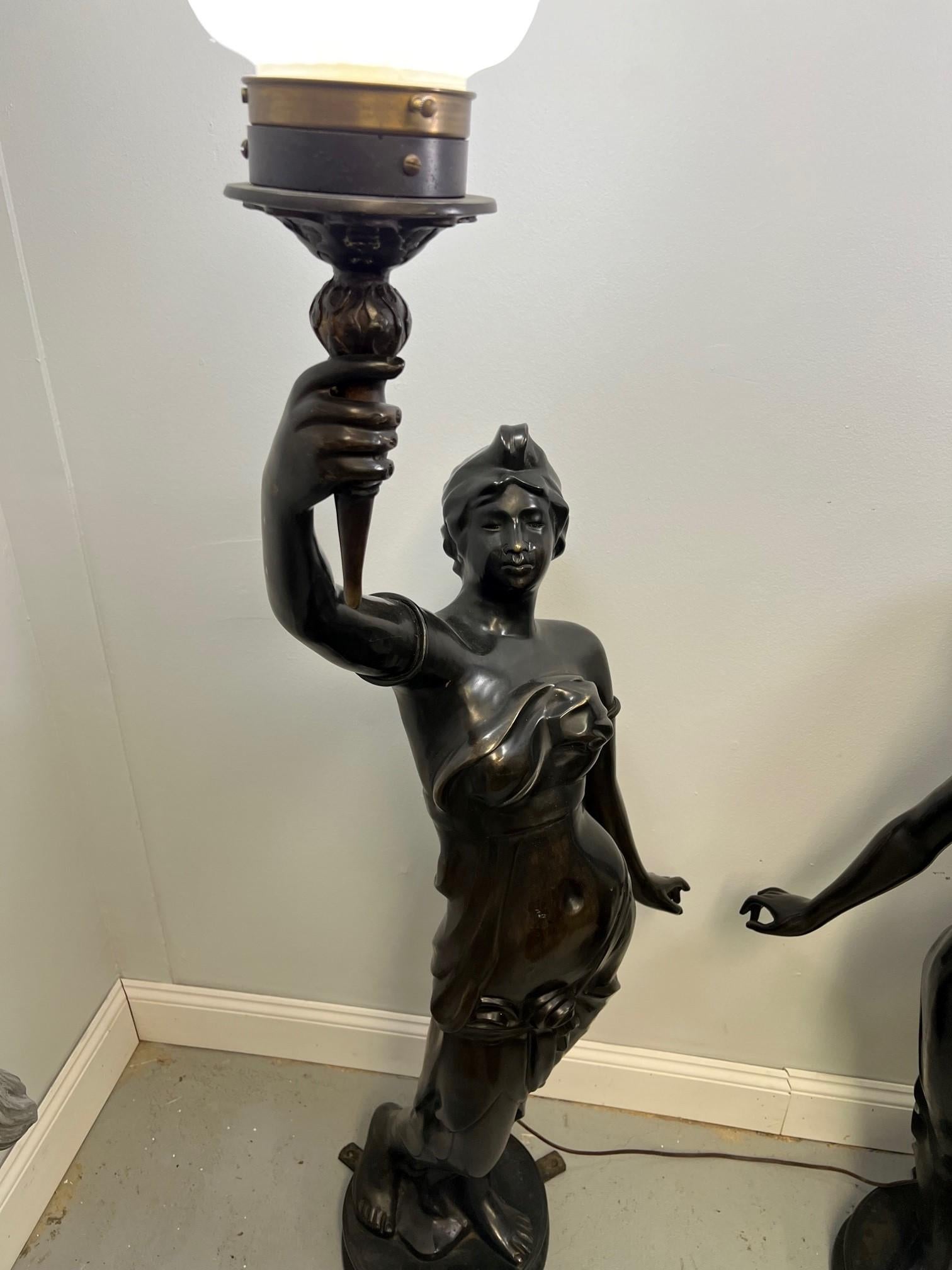 Beautiful pair of bronze figural torchieres of two women holding torches which are electrified. This is a classic pair of draped bronze women holding aloft a flamed torch. The pair was imported to the United States from Thailand known for quality