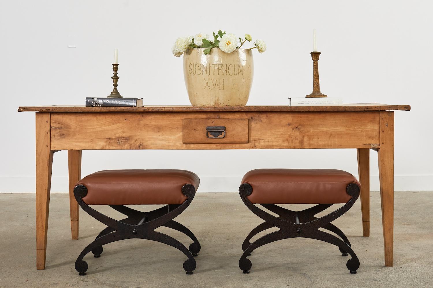 Whimsical pair of iron stools or curule benches featuring terracotta leather seat cushions. The x-form base has a dark bronzed patina powder coat finish that is smooth and textured. Very solid with excellent joinery and craftsmanship. Price is for a