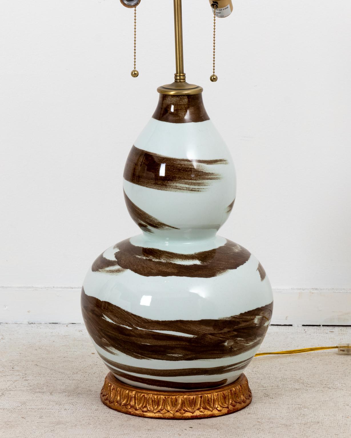 Contemporary pair of brown and white ceramic gourd shaped table lamps by Bunny Williams. The lamps feature brushstroke details on the body, gold giltwood carved bases, and double socket switch. Made in the United States. Shades not included. Please