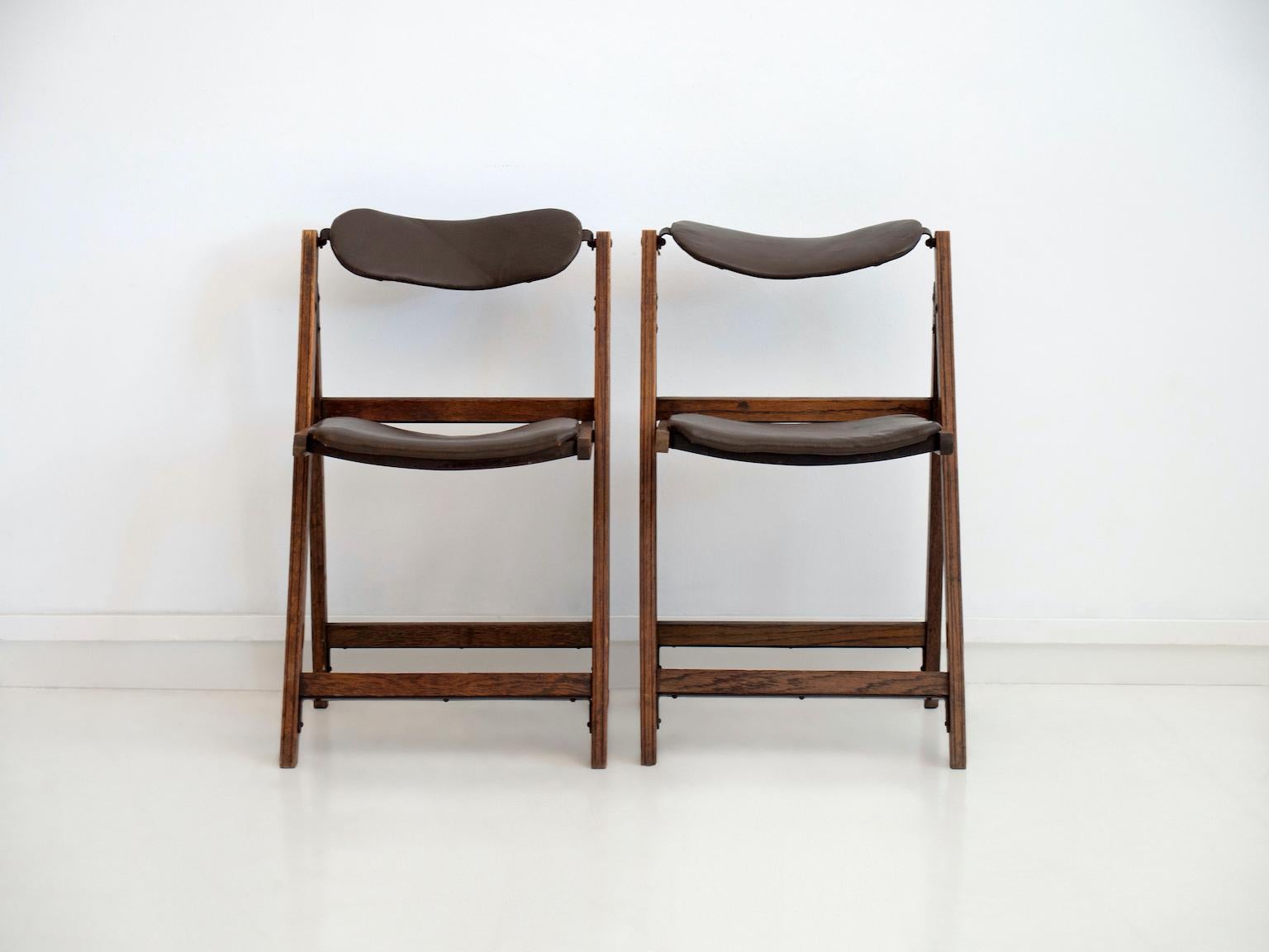 Pair of vintage folding chairs. Frame made of stained oak, brown faux leather covered back and seat. Labeled by the maker.