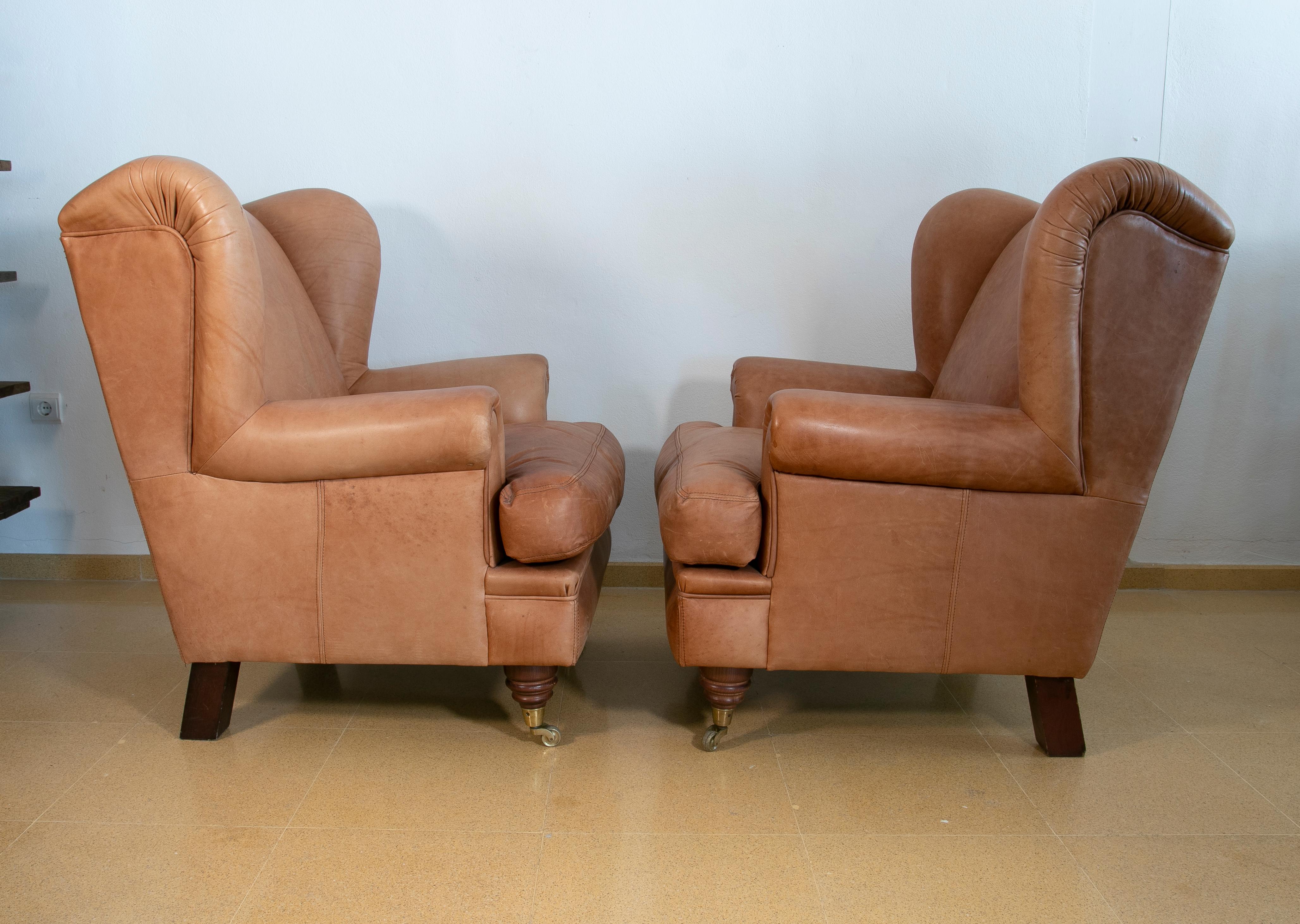 Spanish Pair of Brown Leather Armchairs with Wooden Legs and Brass Wheels For Sale