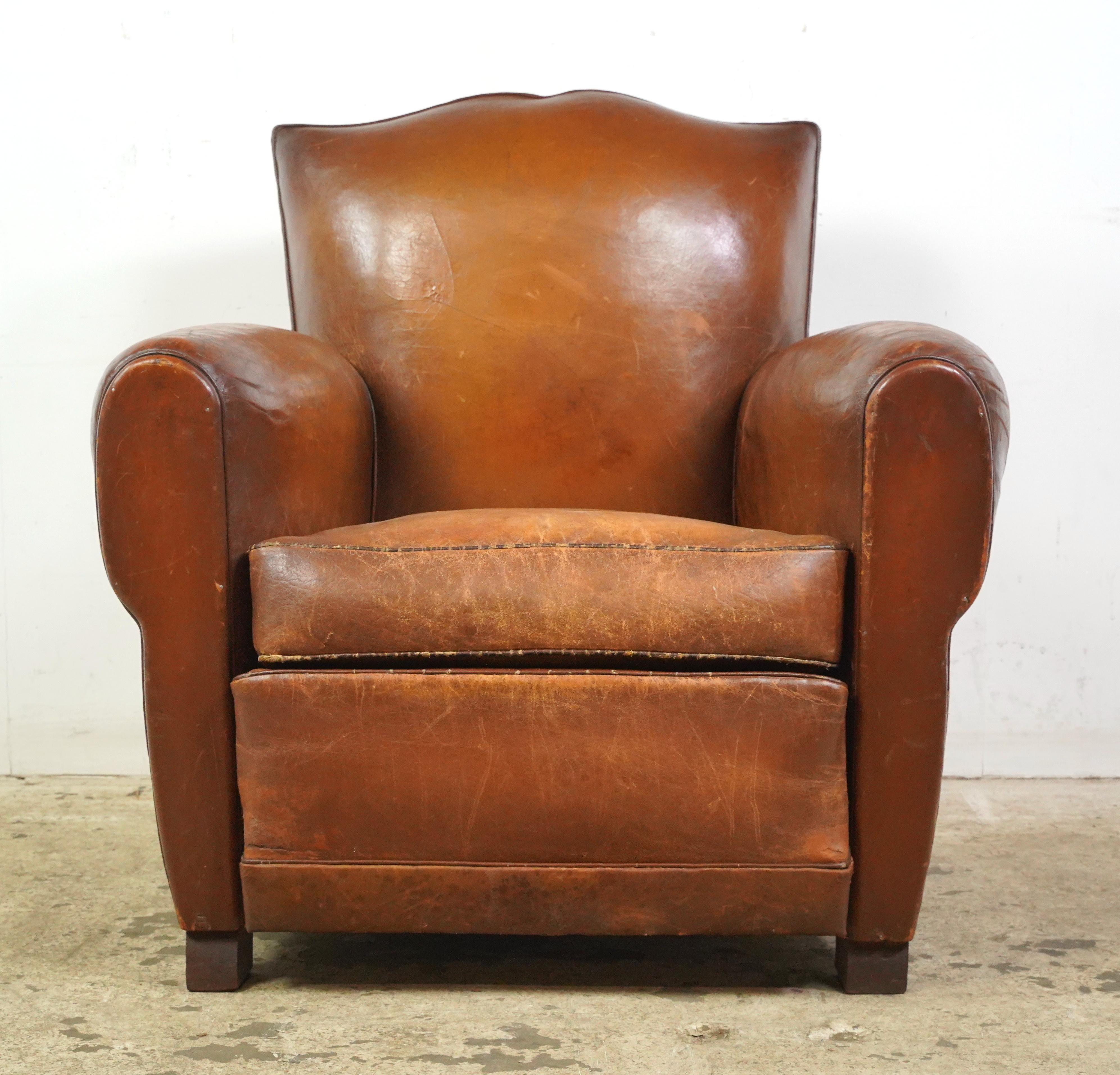 Mid-Century Modern style leather dining chairs made in France. The chairs have a distinct shape with a slightly angled back and a seat that appears to be wide, and black painted wooden legs. The leather and feet show signs of wear and age. Please
