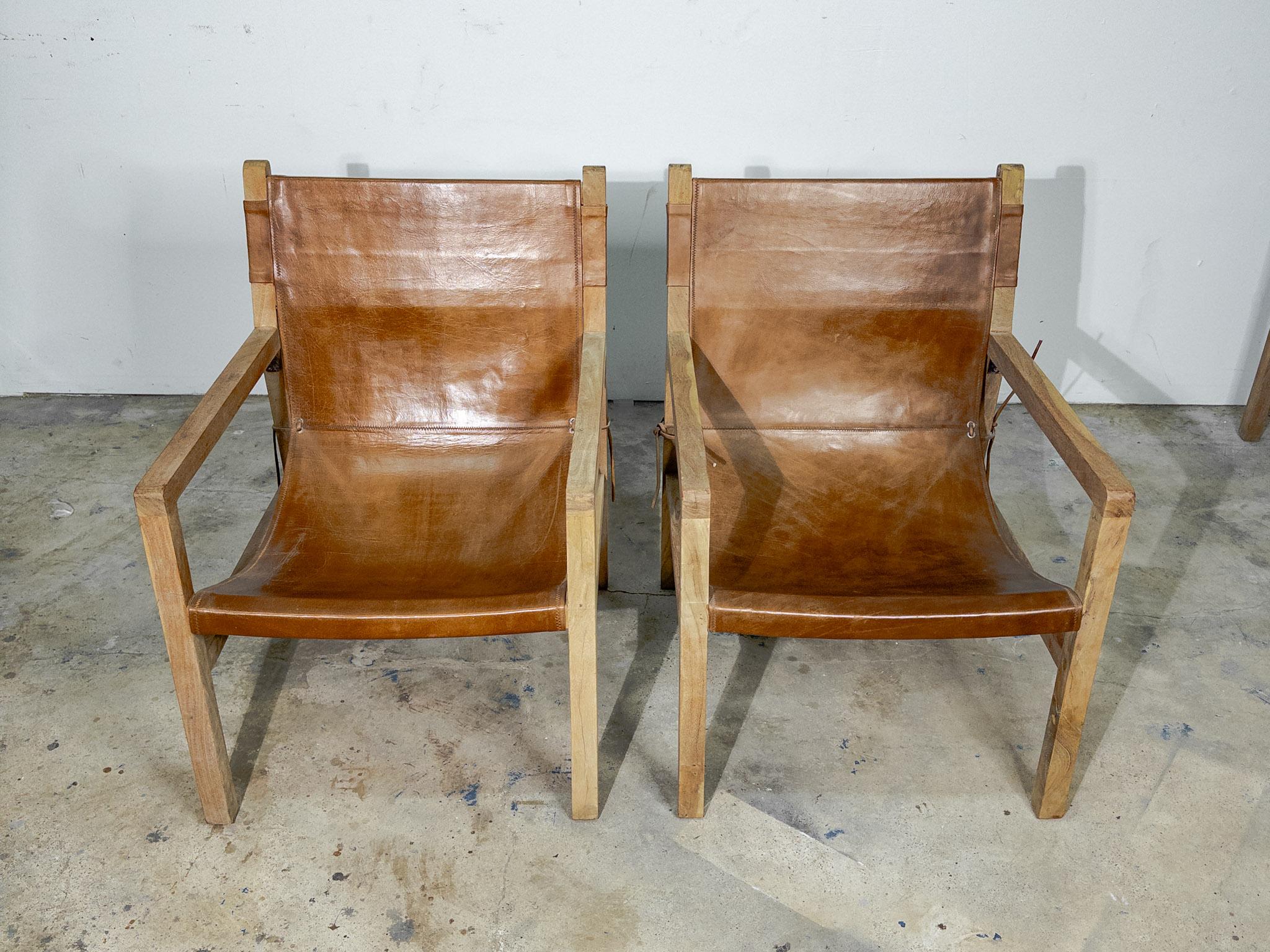 The pair of brown leather sling chairs presents a striking combination of modern elegance and rustic charm. Each chair features a rich, supple brown leather seat and backrest, exuding luxury and comfort. The leather, aged to a perfect patina, is