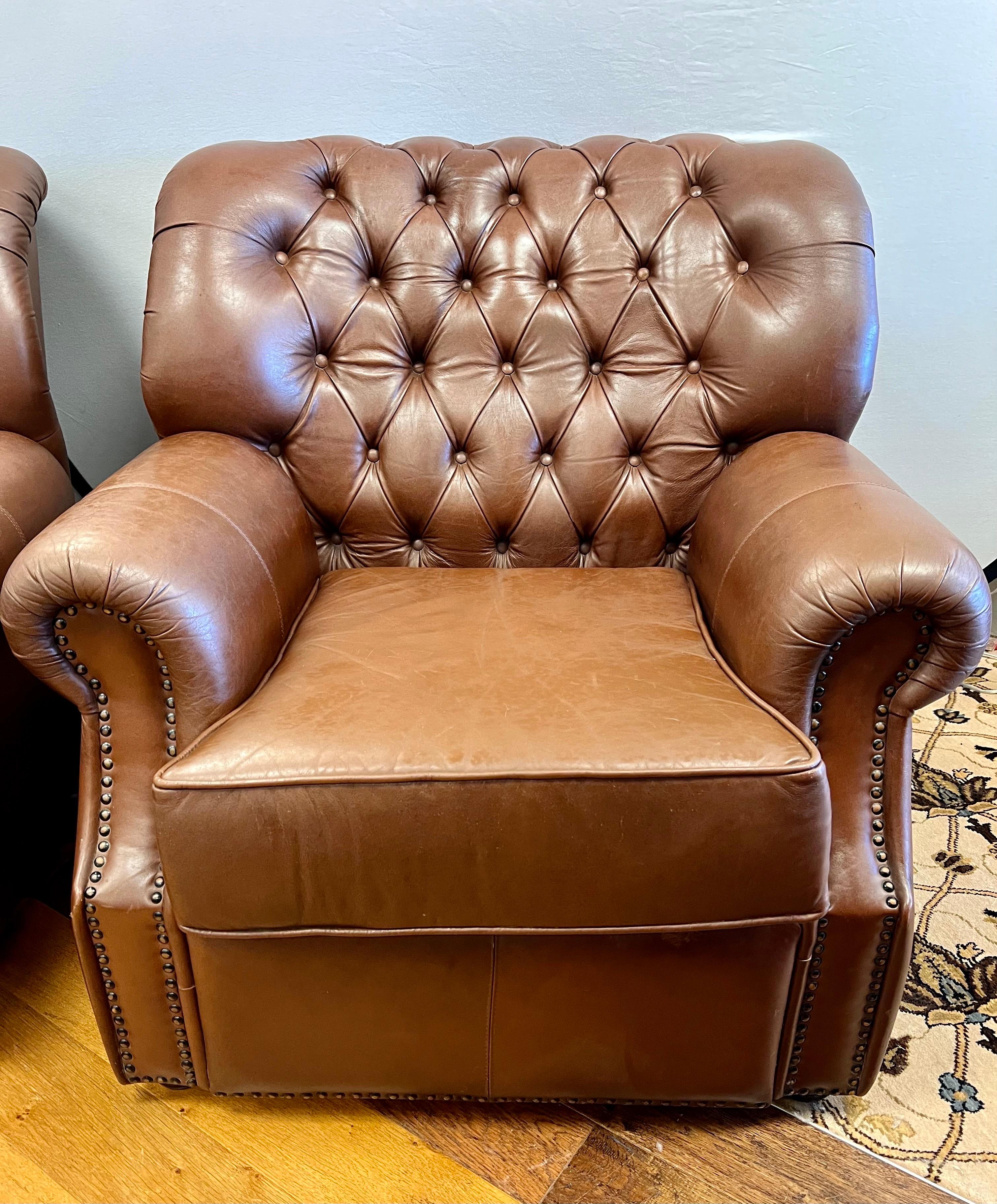 Handsome matching pair of oversized brown leather button tufted club chairs with nailhead trim. Boasting big oversized dimensions, a wide tufted concave back, eight way hand tied construction and rolled arms. Their size and craftsmanship make them