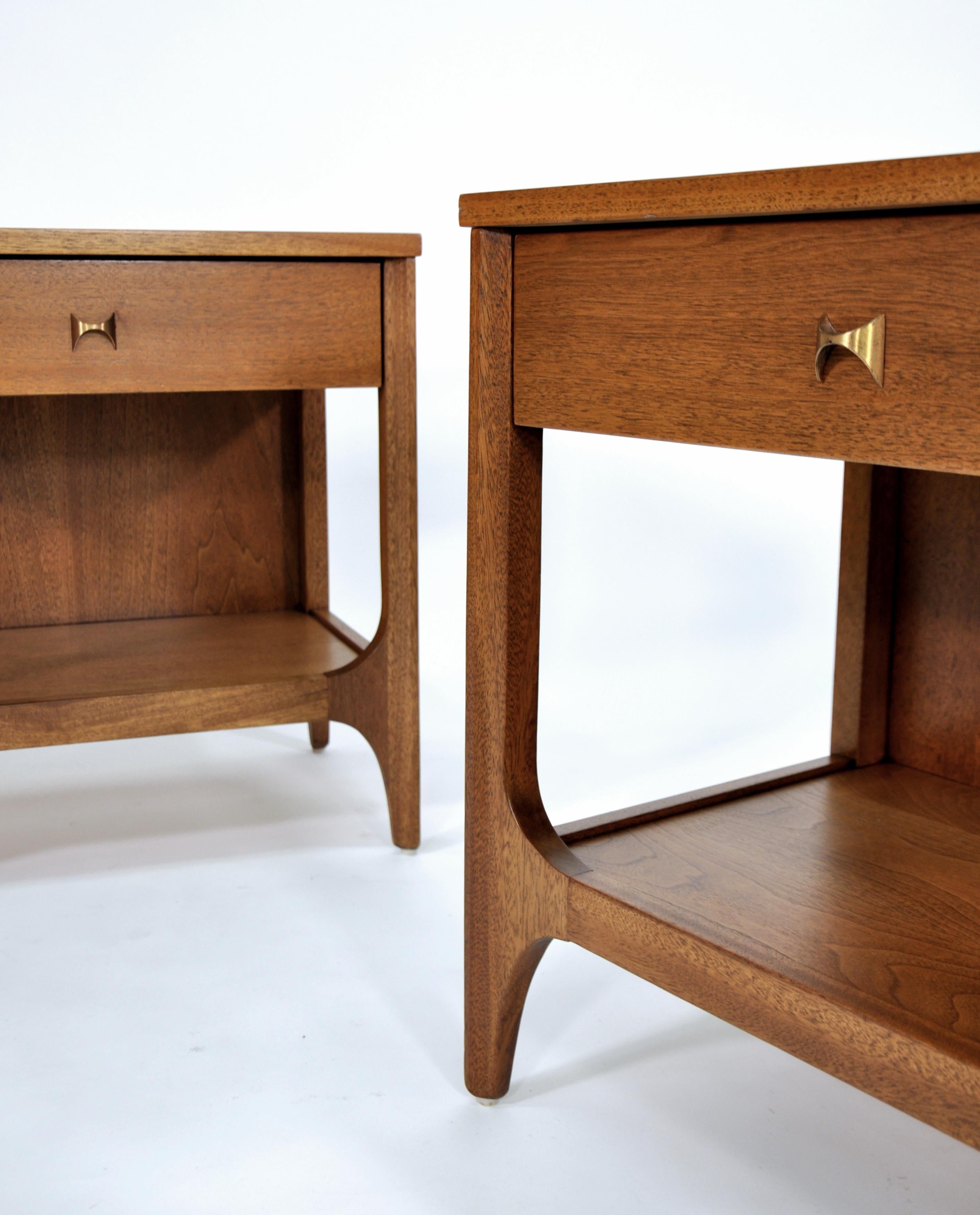 Pair of vintage Mid-Century Modern walnut and brass end or bedside tables from the Brasilia II line manufactured by Broyhill in the 1960s. Each two-tiered occasional table is fitted with a drawer and a shelf. The drawer fronts of the nightstands