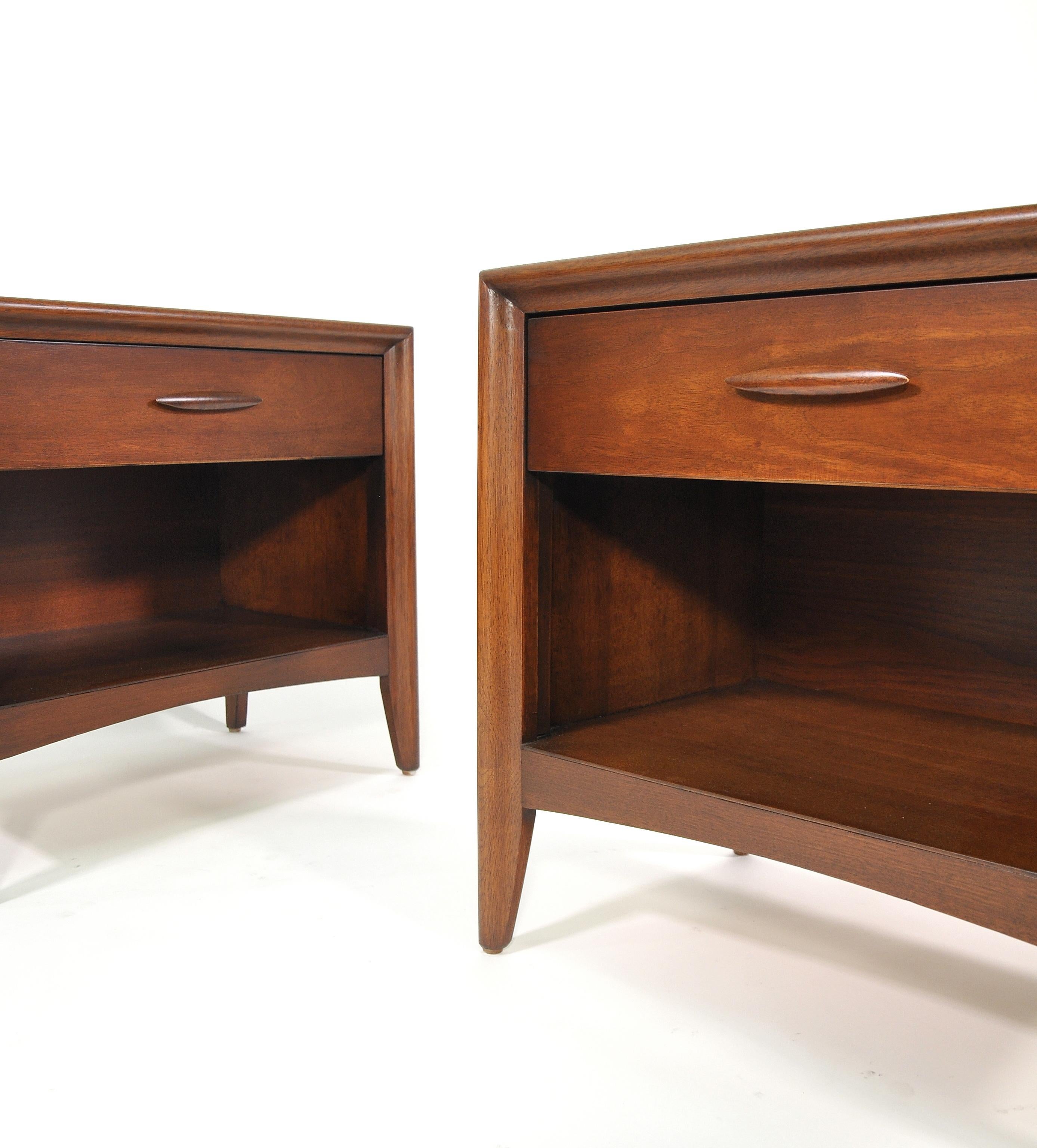 Pair of vintage Mid-Century Modern walnut end or bedside tables from the Emphasis line manufactured by Broyhill in the 1960s. Each two-tiered occasional table is fitted with a drawer and a shelf. The drawer fronts of the nightstands have the