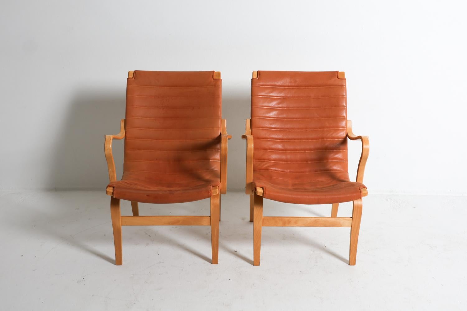 Si tratta di un'iconica coppia di poltrone lounge nota come modello 'Eva', disegnata da Bruno Mathsson per DUX. Realizzate in legno di faggio con la tecnica del legno curvato, le sedie 