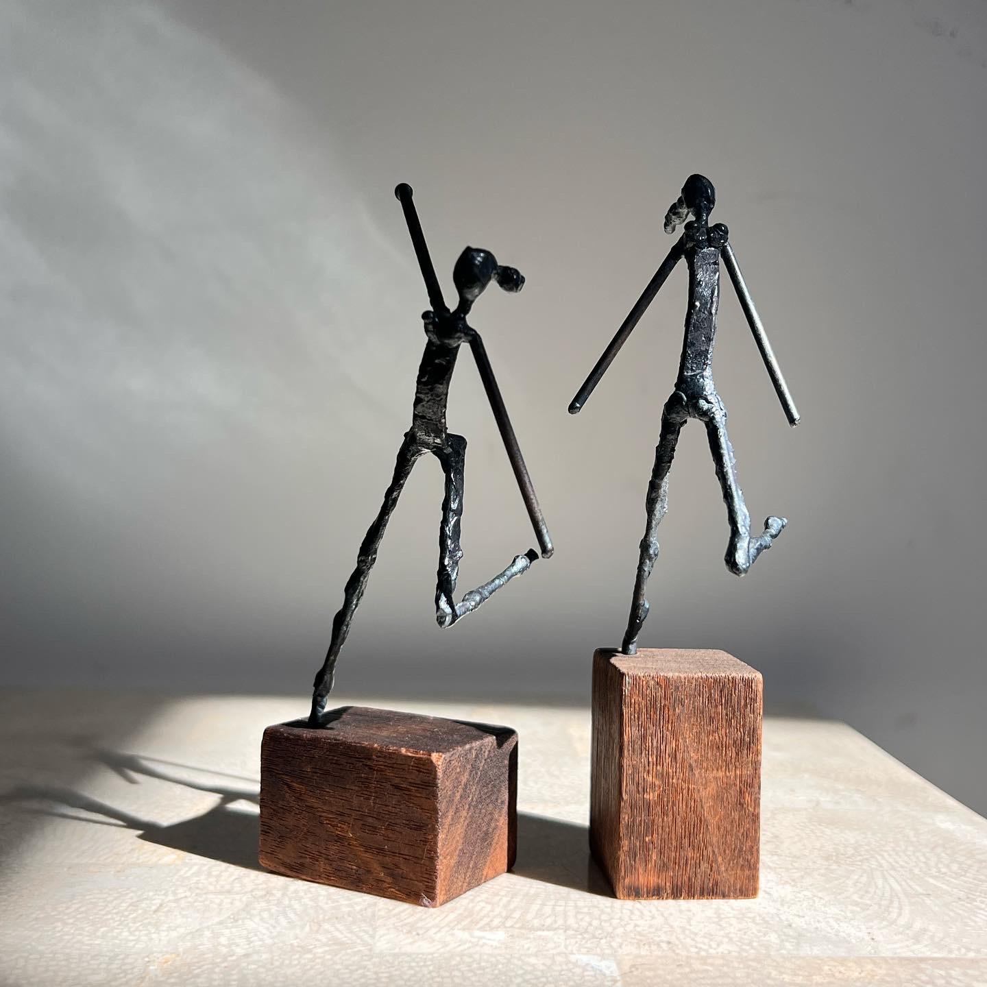 A pair of brutalist figurative sculptures by Arturo Bassols, signed by artist, 1968. Welded hand-worked metal and walnut wood, and each displaying a femme figure in mid-movement. Bassols (1932-2001) was a Cuban American artist who worked primarily