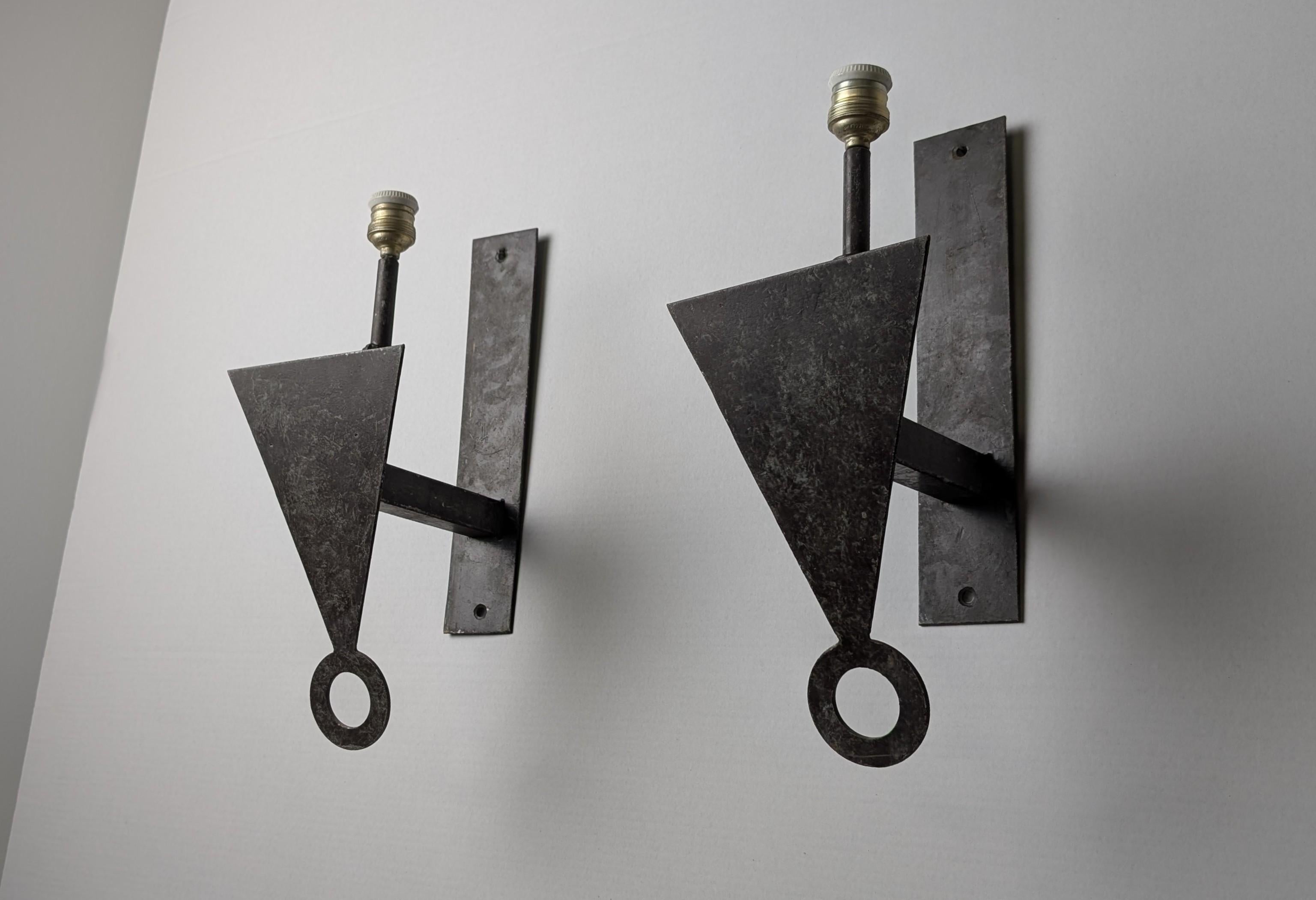 Coppia di appliques definite da un chiaro profilo geometrico caratteristico dello stile brutalista degli anni '70. Realizzato in metallo, il design è caratterizzato da un triangolo rovesciato che costituisce lo scudo principale dell'applique. Un