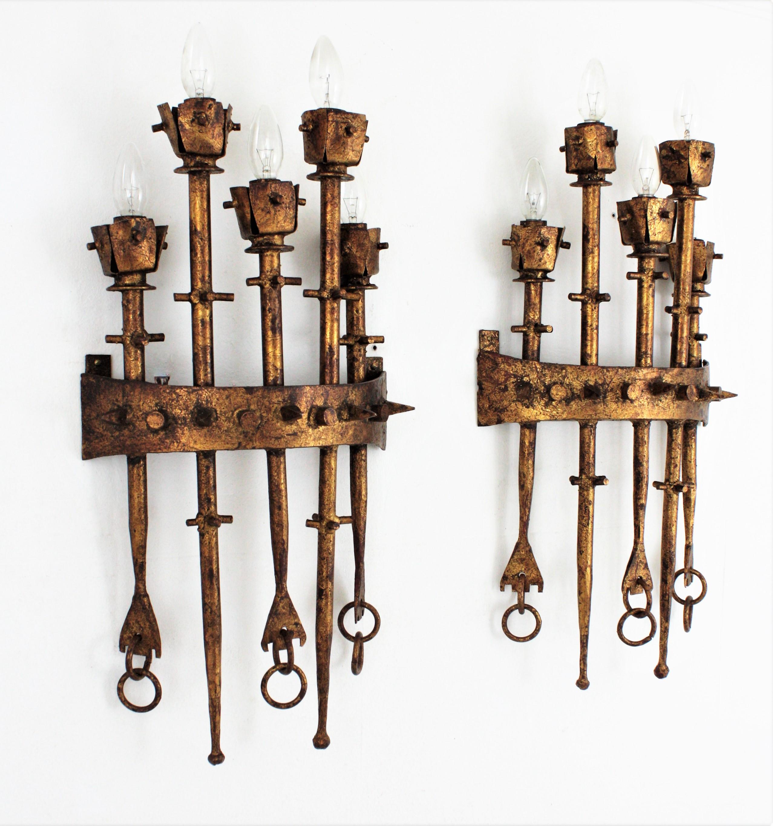 Outstanding pair of hand forged five-light gilt iron torchère wall lights. Spain, 1940s-1950s.
These wall sconces were handcrafted with an excellent metal work and Gothic / medieval inspired design. The five torch lights are featured in different
