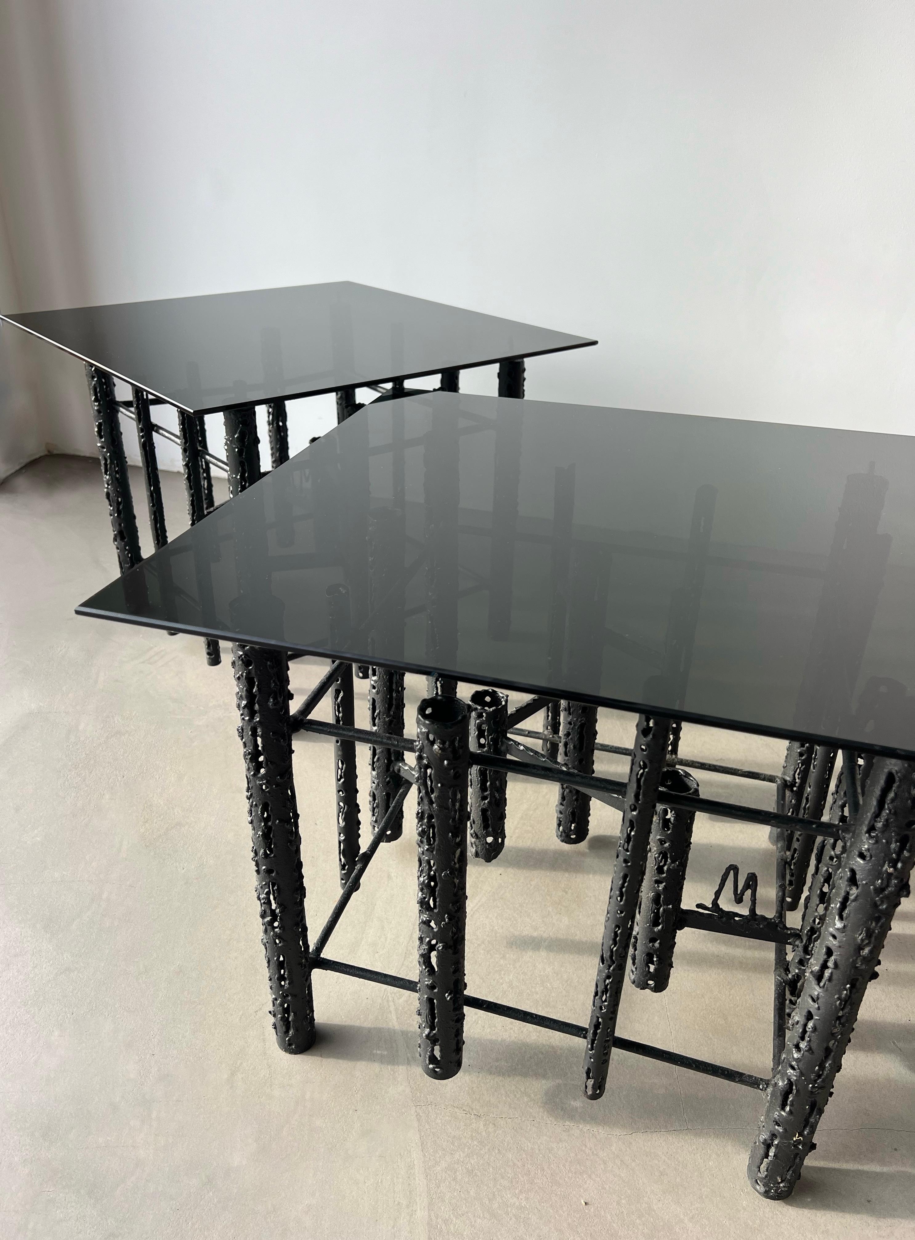 Ces étonnantes tables d'appoint brutalistes de Masciarelli pour Regent, fabriquées dans les années 1960, présentent des bases métalliques cylindriques texturées et torchées, créant un jeu d'ombres et de lumières visuellement fascinant. Leurs formes