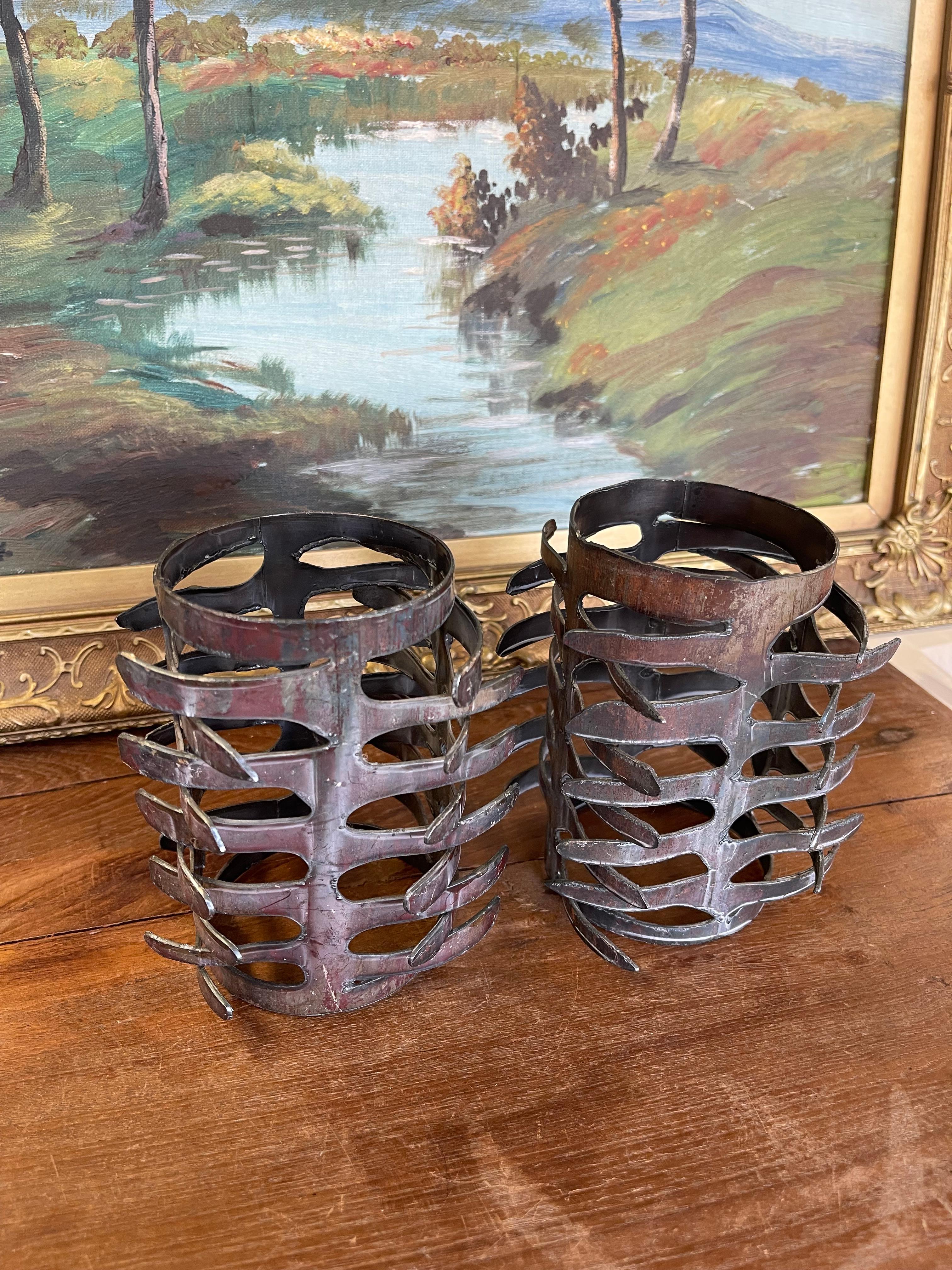 Dieses Paar skulpturaler Kerzenhalter zeigt ein markantes brutalistisches Design, das aus handgeschnittenem und geschweißtem Metall mit industrieller Patina gefertigt ist. Jedes Stück hat eine zylindrische Form mit geschichteten, ausgeschnittenen