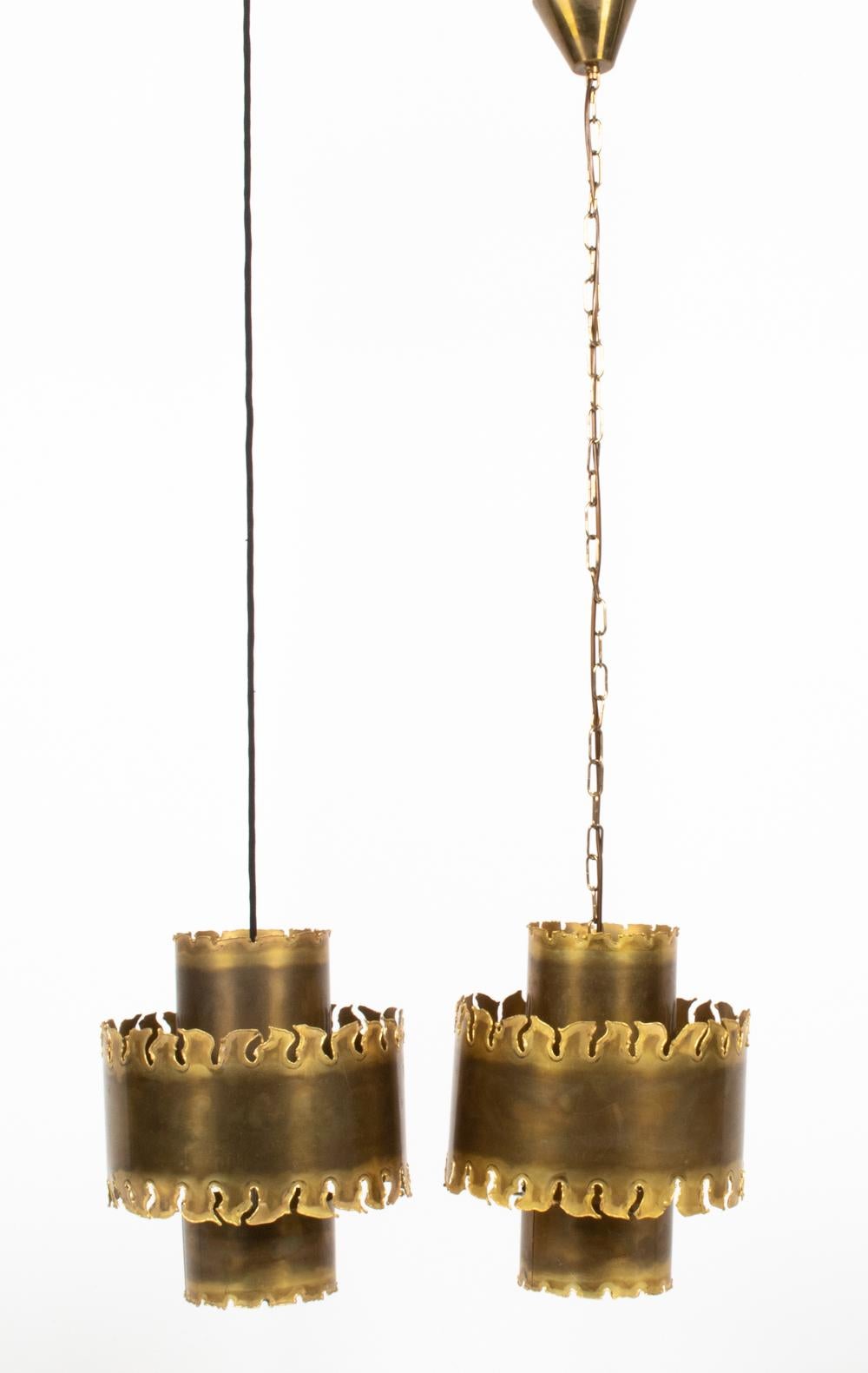 Transform your space with this striking pair of pendant lights in patinated and torch-cut brass, whose dramatic flame-like edges evoke the very implement with which they were formed. Designed and produced by the famous Danish lighting firm Holm