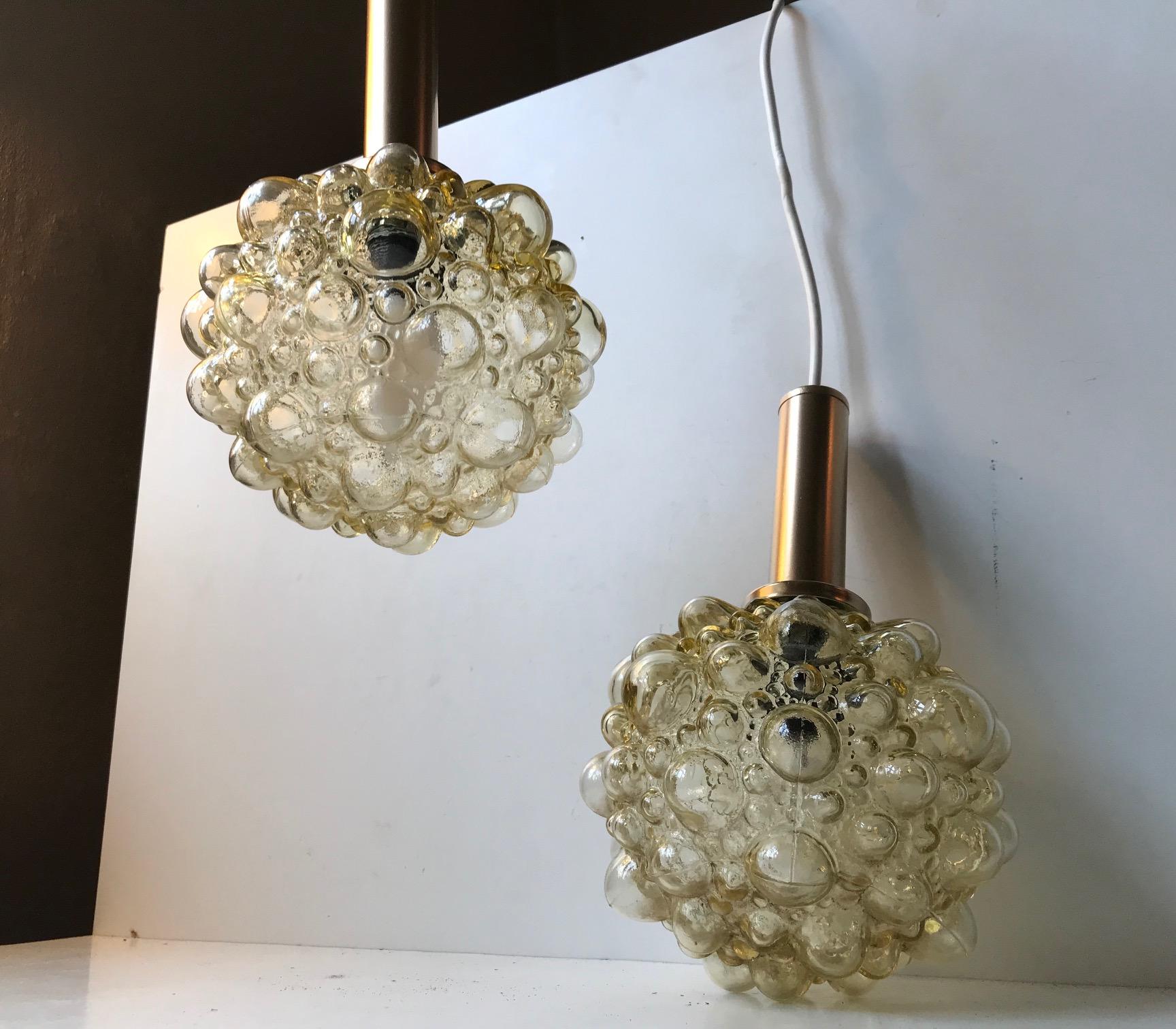 These round smoke tone amber bubble glass pendant lamps was designed by Helena Tynell for Limburg, and manufactured in Glashütte, Germany during the 1960s. The golden top's may have been re-lacquered at some point.