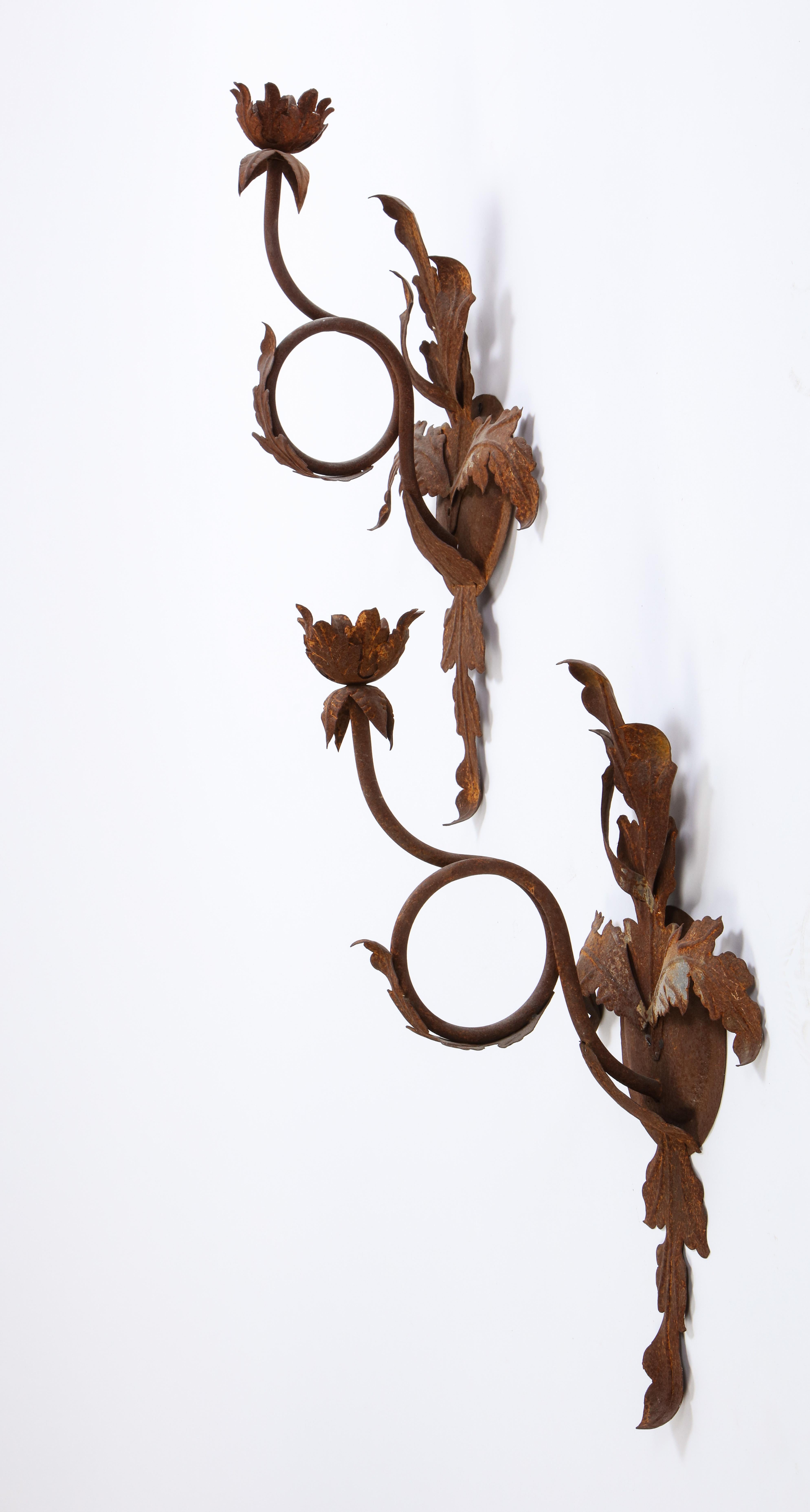 A pair of 20th century wrought-iron wall lights or sconces with rust patina and floral motif. Each sconce is formed as a budding flower with leaf-form pendants.

Property from esteemed interior designer Juan Montoya. Juan Montoya is one of the most