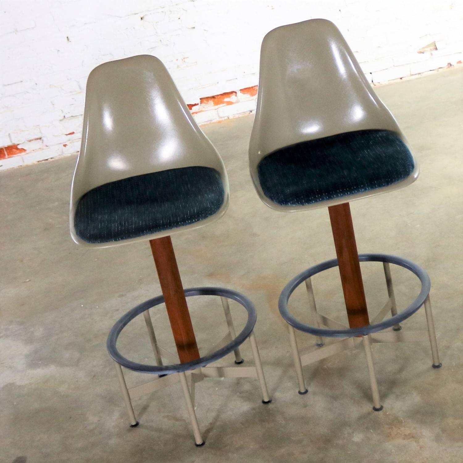Handsome and iconic pair of Mid-Century Modern swivel bar stools with footrest and upholstered seat pad by Burke, Inc. This pair is in wonderful vintage condition. They would be better served if the fabric were replaced; however, they are usable as