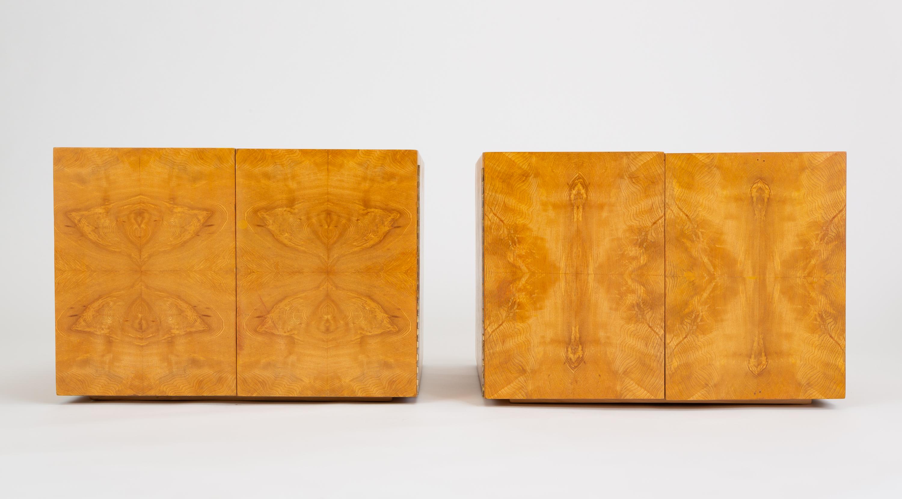A versatile pair of storage pieces or side tables have a simple design, distinguished by the highly figured, bookmatched burl wood that decorates their surfaces. The front of each pieces opens at two plain-faced doors with hidden magnetic latches.